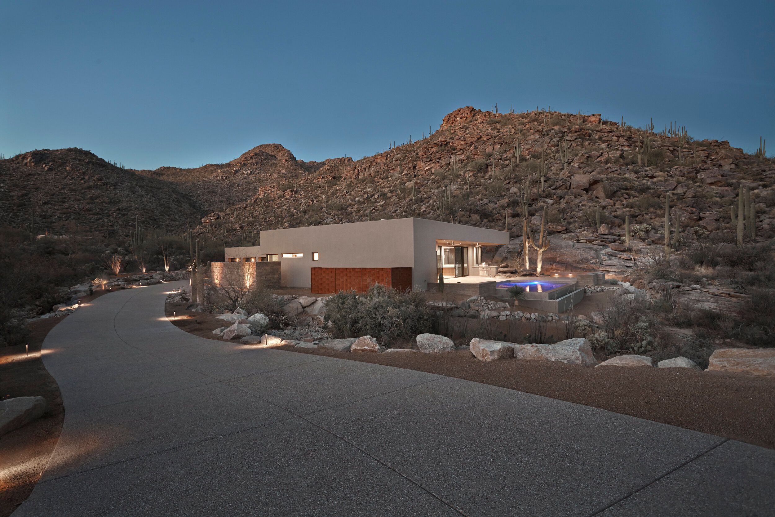 Contemporary desert home at dusk set beneath a boulder-strewn hillside