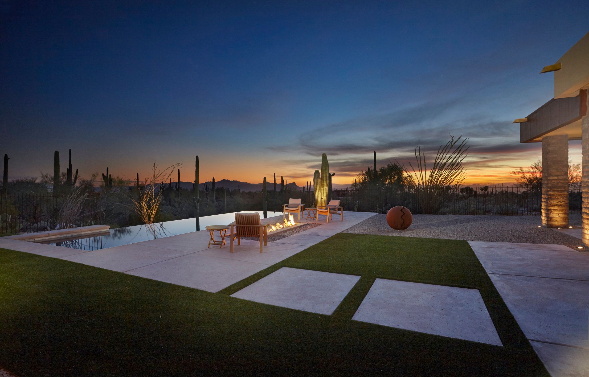 Negative-edge pool and lawn at sunset with saguaros silhouetted on the horizon