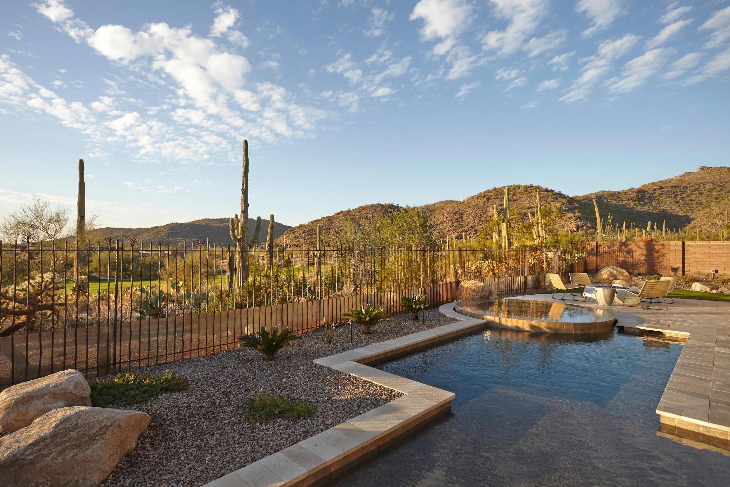 Pool and raised spa on a paver deck with saguaros and hills beyond