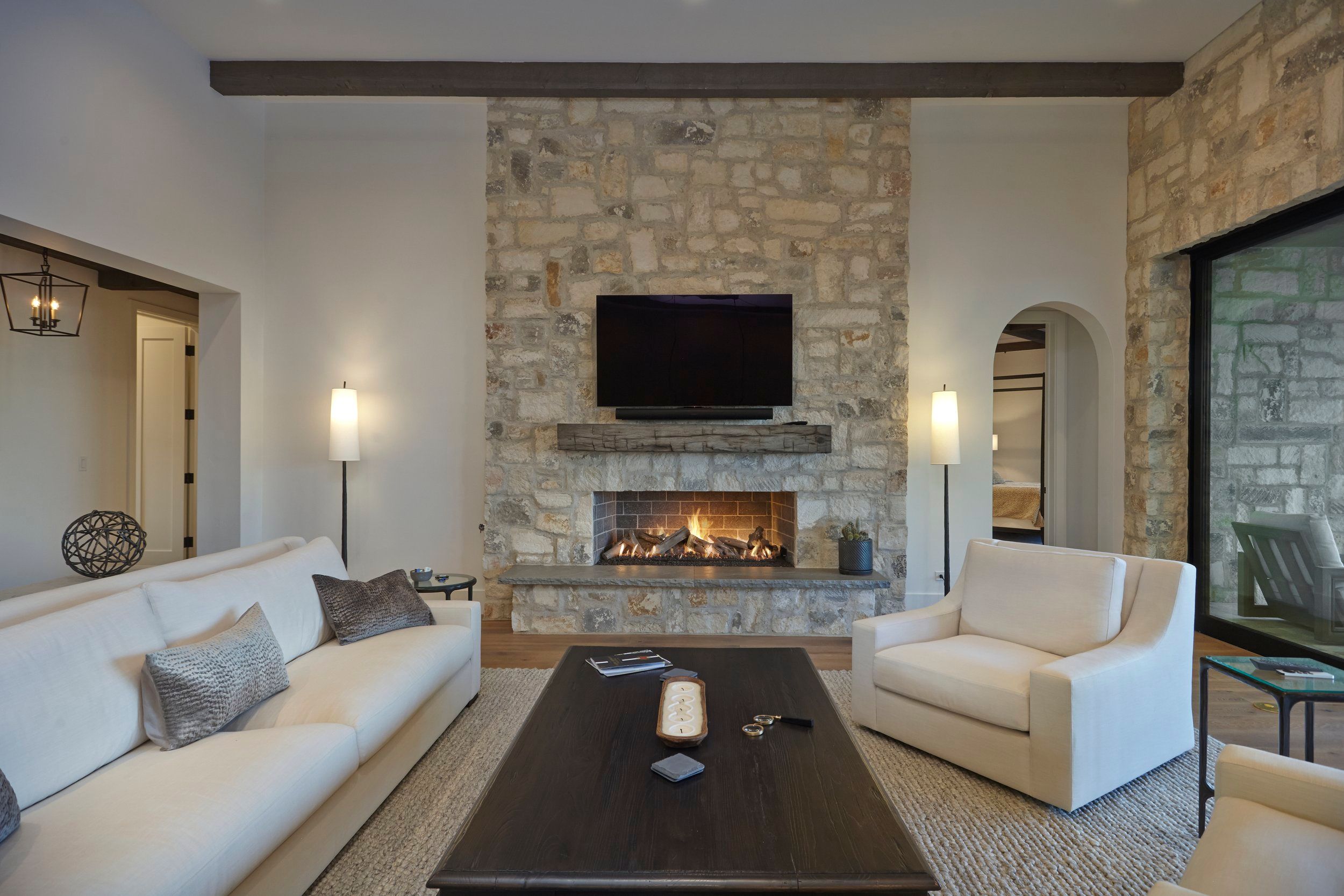 Living room with a stone fireplace, mounted television and white upholstered seating