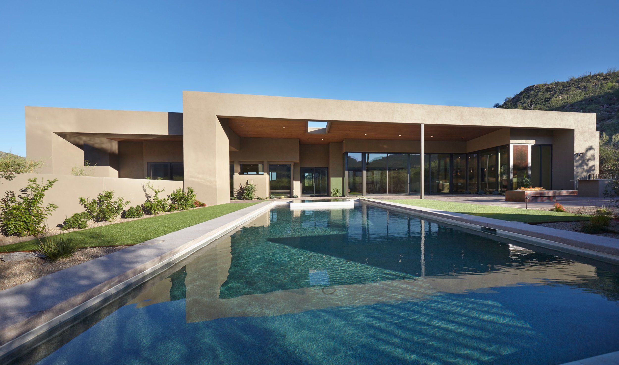 Contemporary flat-roofed home with a long lap pool and lawn under a clear sky