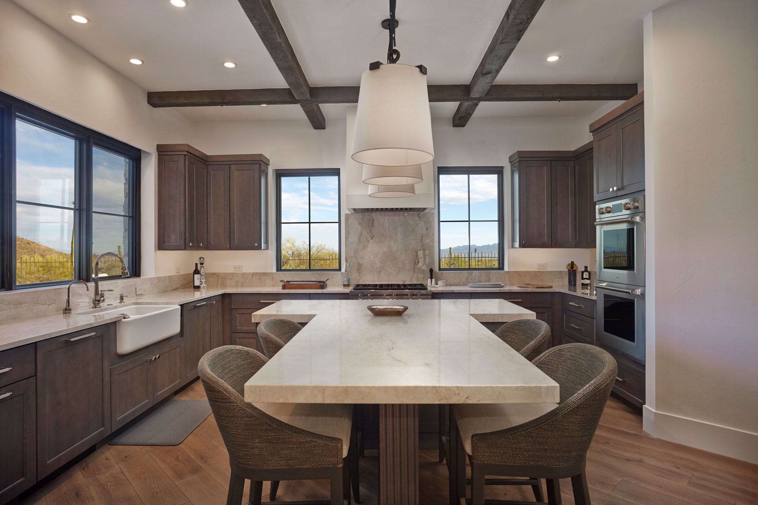 Kitchen with dark cabinetry, farmhouse sink and a long stone island with seating