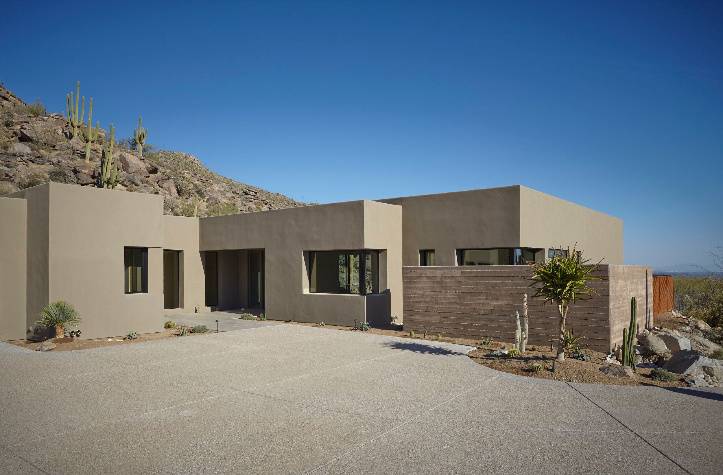 Flat-roofed stucco and timber elevation against boulders and saguaros