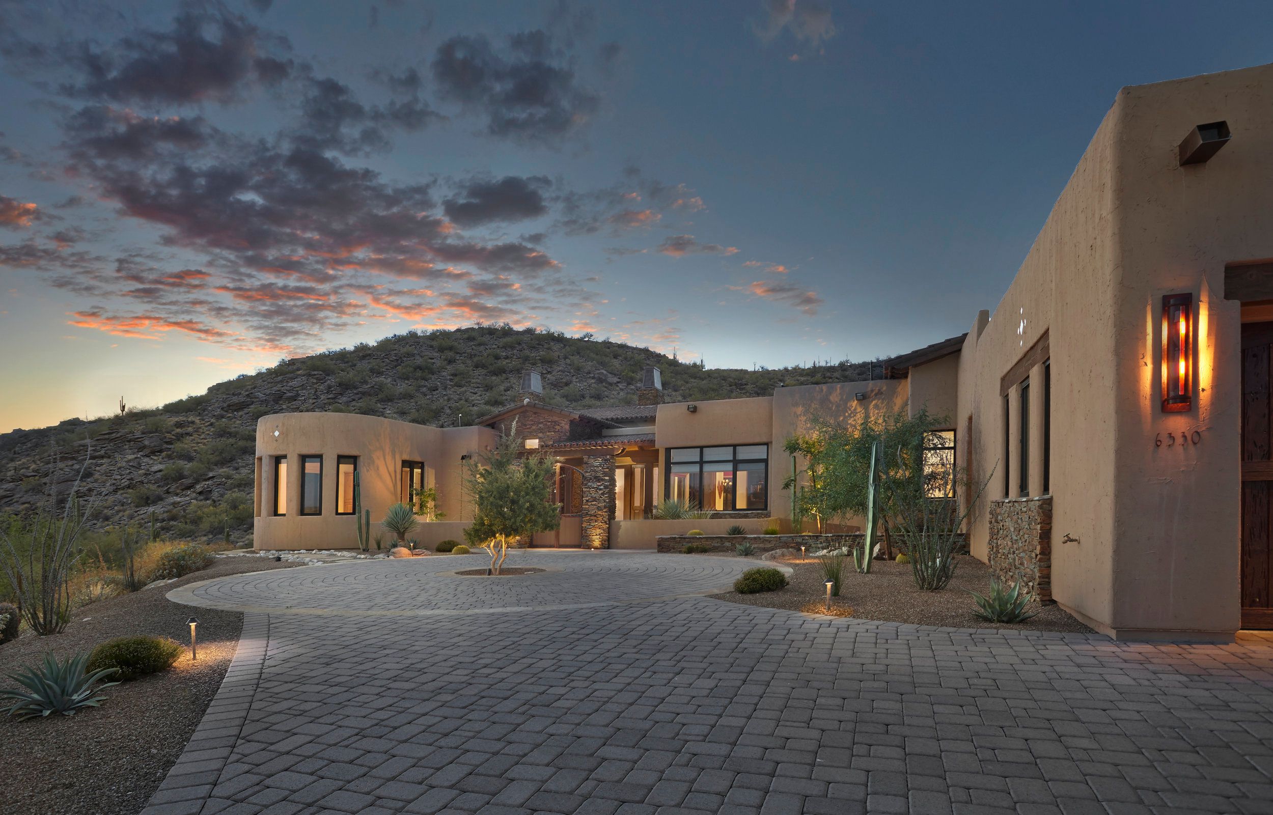 Front elevation and paver motor court at dusk beneath a desert hillside