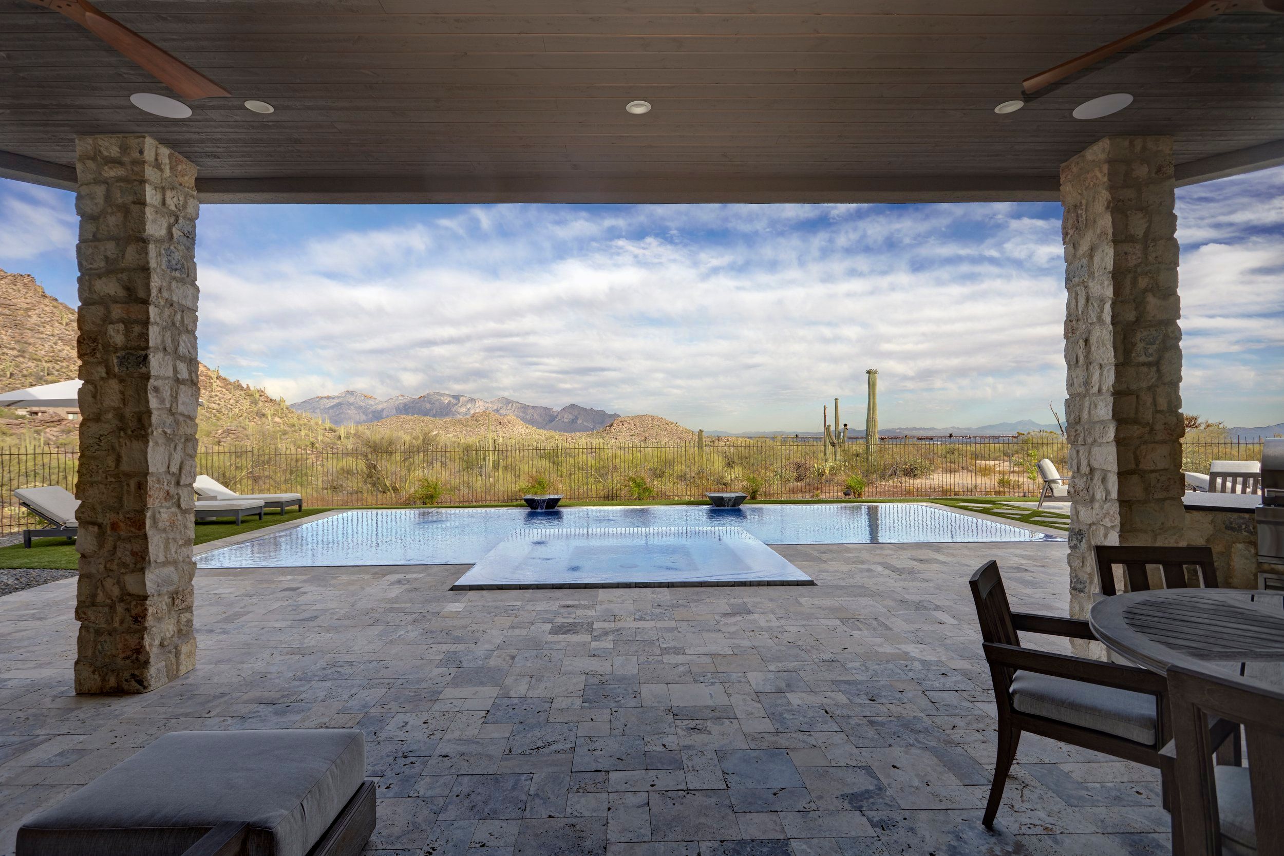Covered patio framed by stone columns looking out to a negative-edge pool and mountains