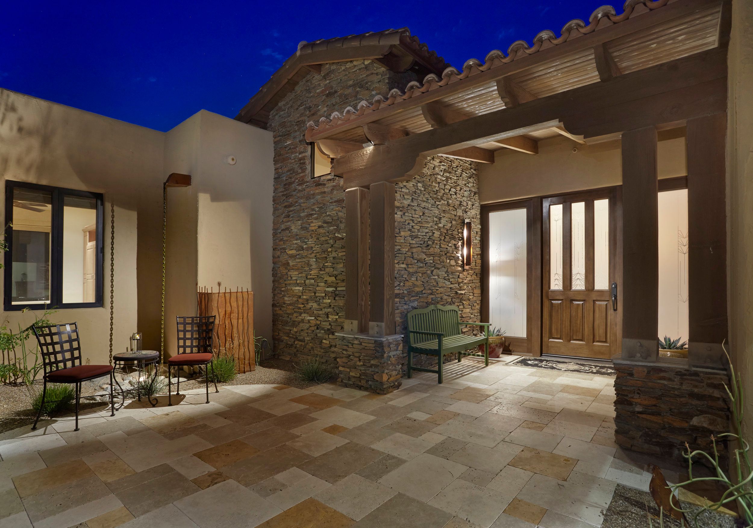 Stone entry portico with timber posts and a paver courtyard at dusk