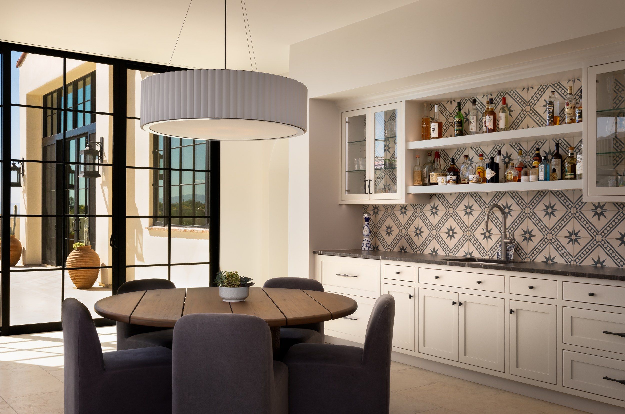 Breakfast table beside a bar with patterned tile backsplash and open shelving