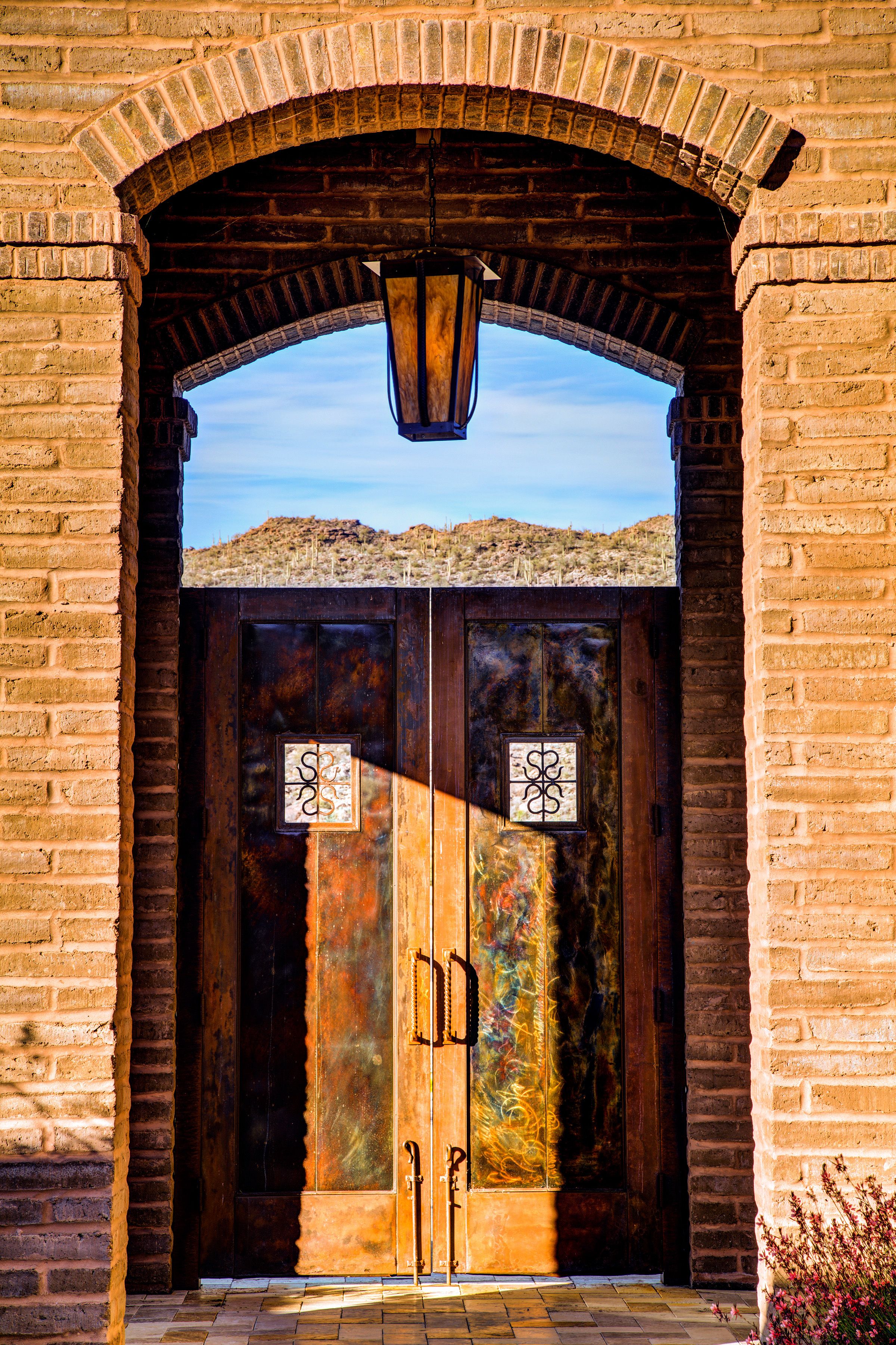 Arched brick entry with patinated copper double doors and a hanging iron lantern