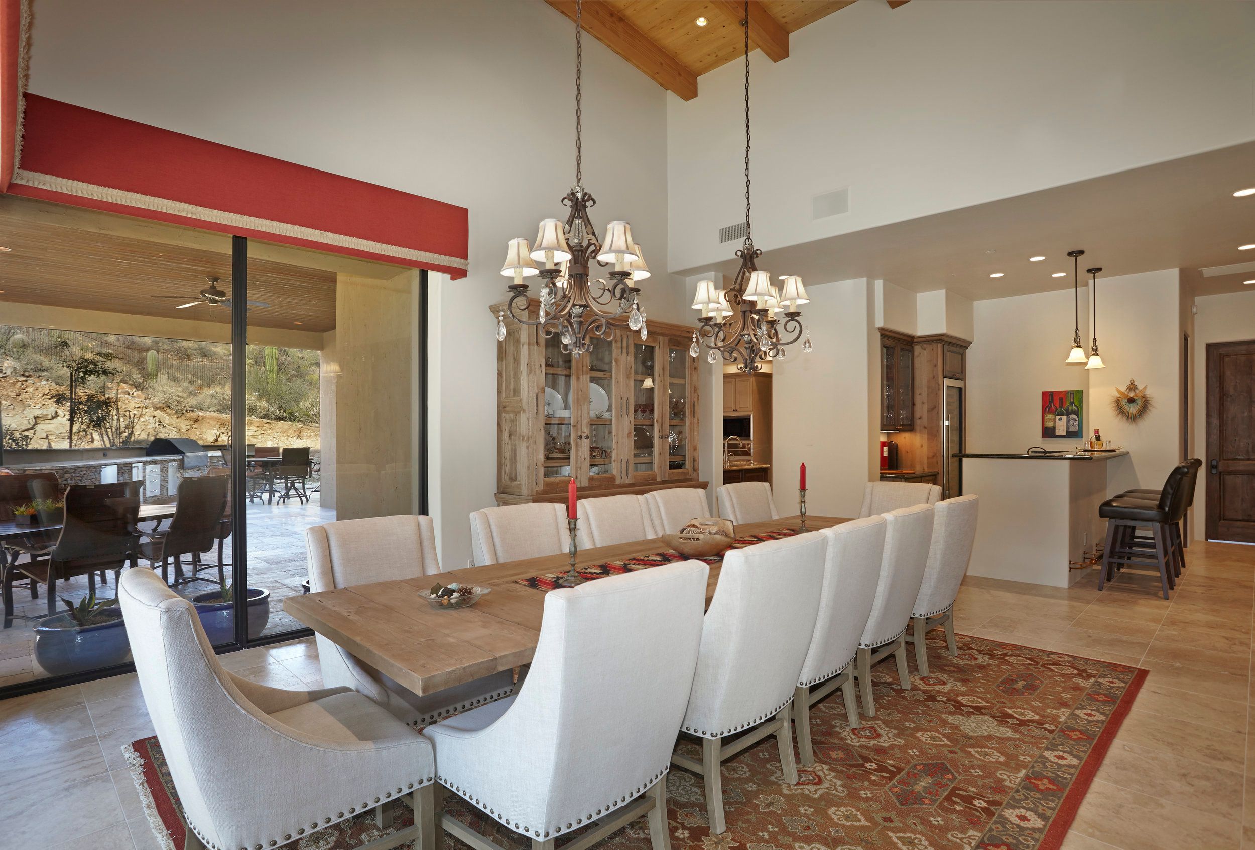 Long dining table with upholstered chairs beneath twin chandeliers