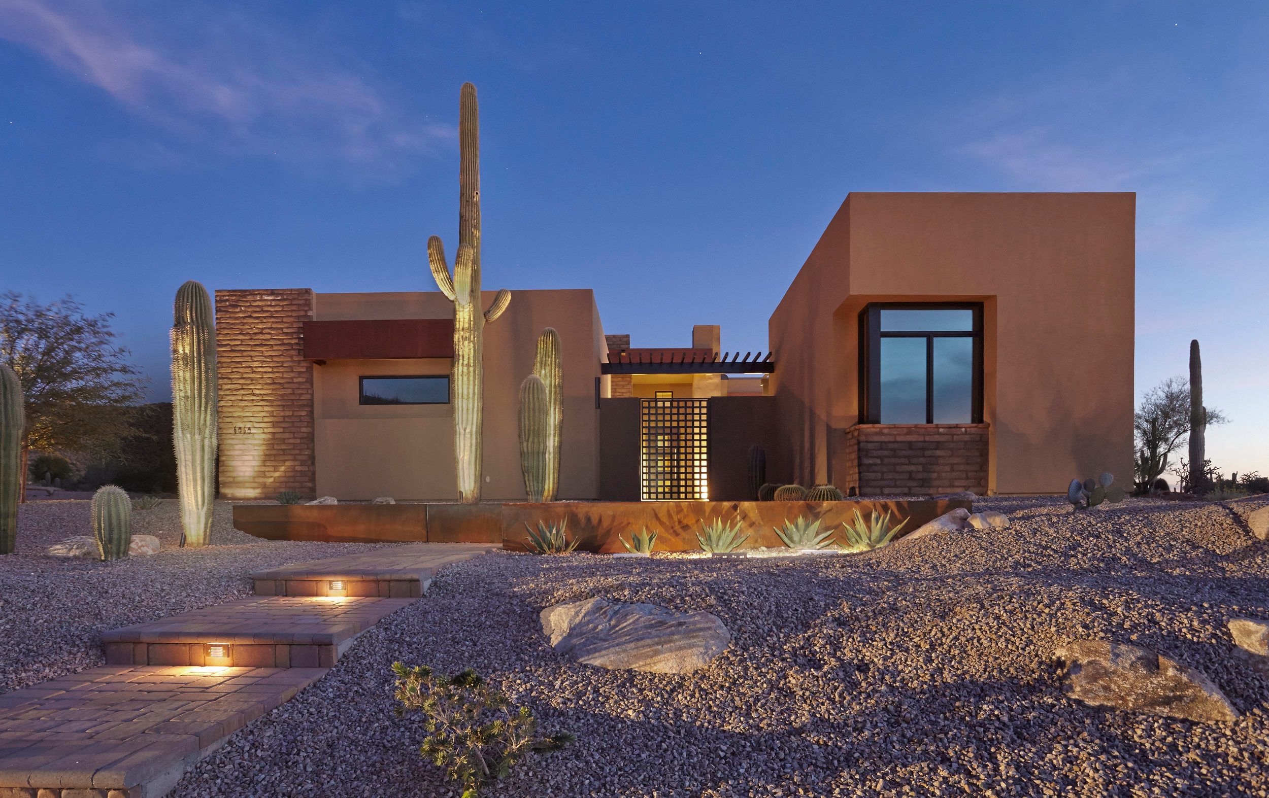 Contemporary adobe elevation with a saguaro and brick screen at dusk