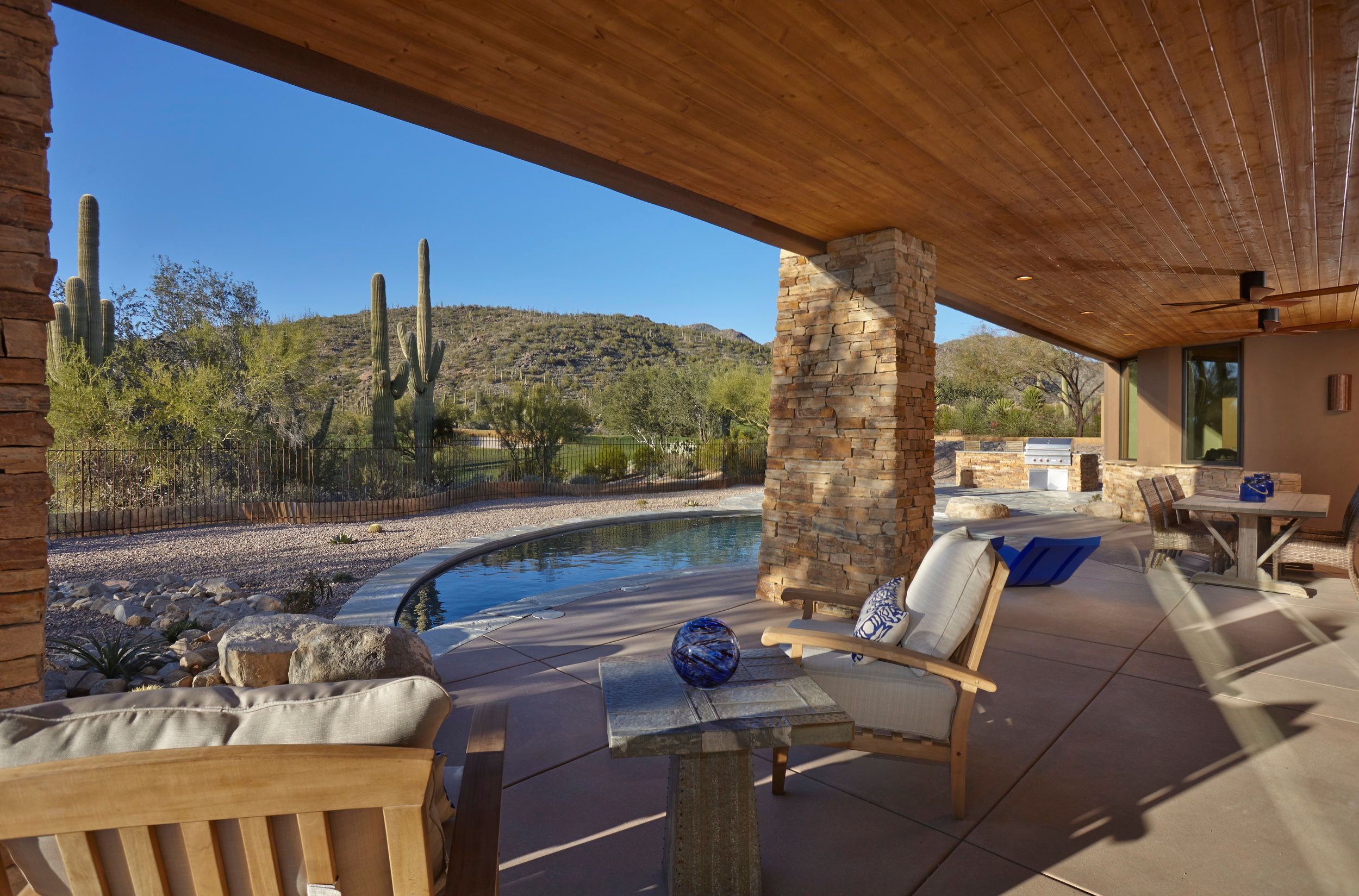 Patio seating beneath a wood-plank ceiling beside the pool and mountain view