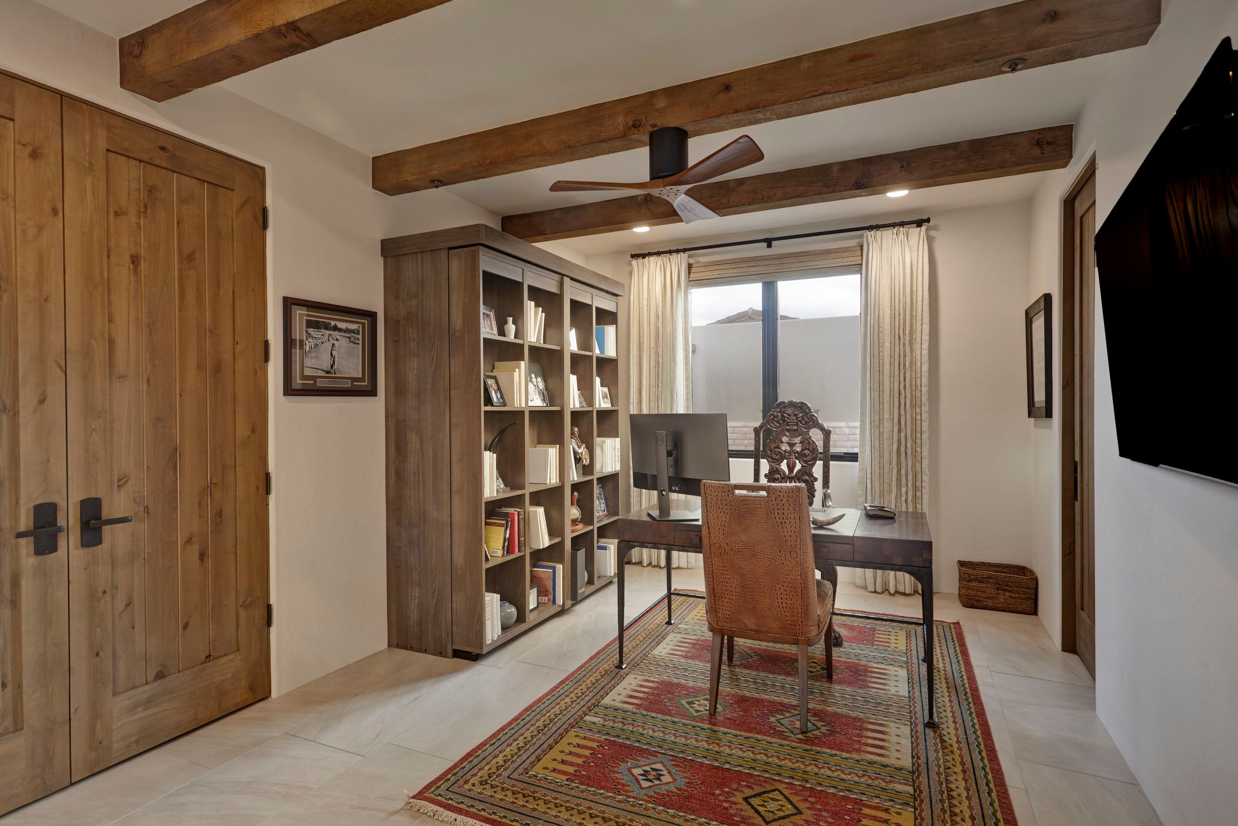 Study with built-in bookshelves, a beamed ceiling and a patterned wool rug