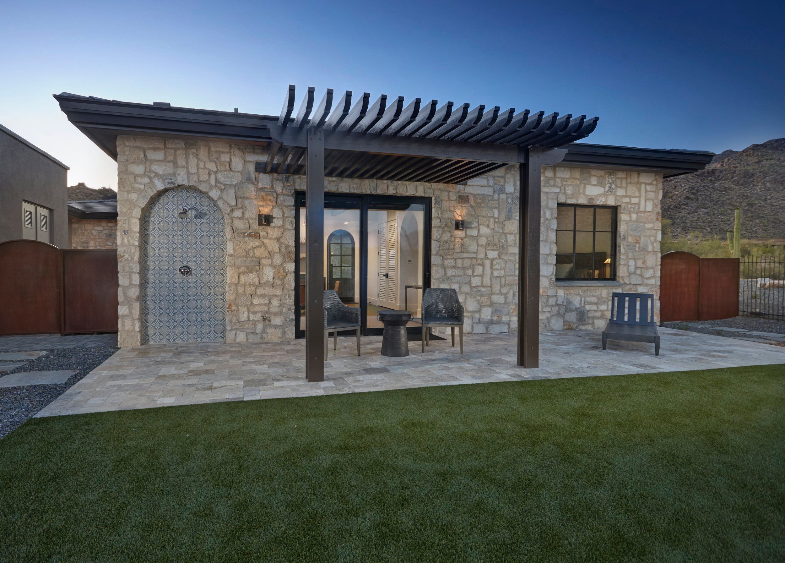 Stone guest casita entry with a timber pergola and lawn