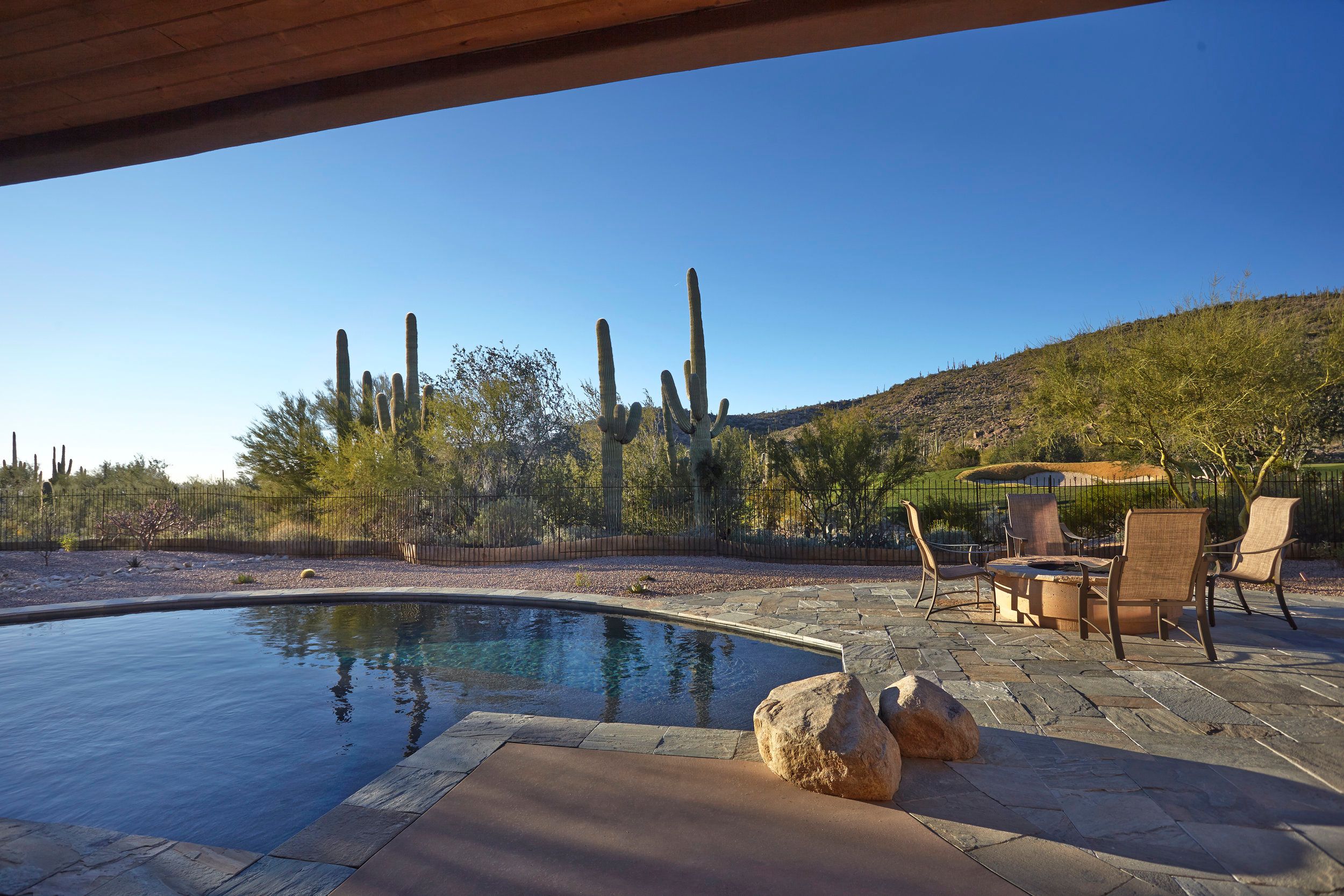 Pool and flagstone deck with saguaros and hills under a clear sky