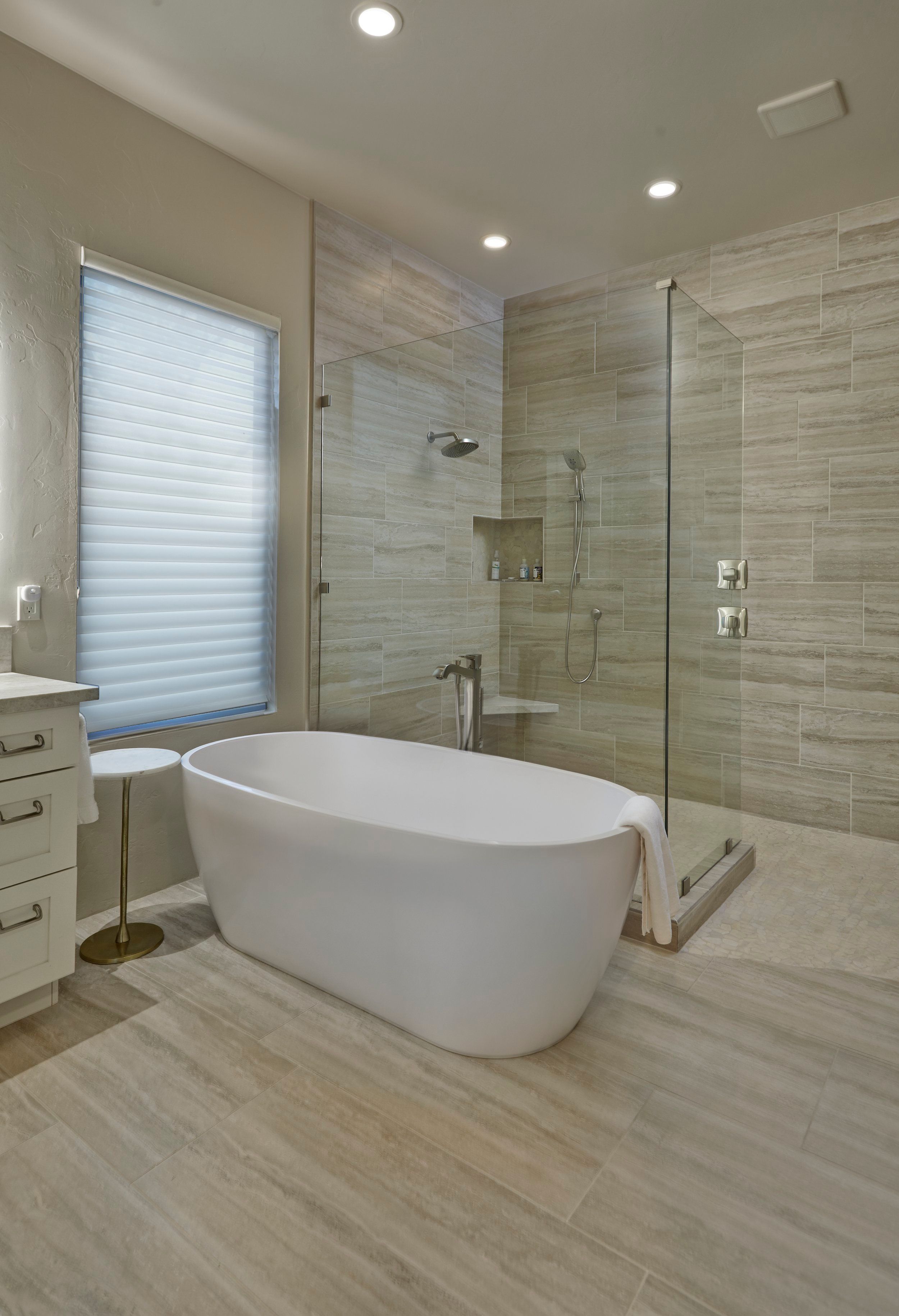 Freestanding tub beside a glass shower enclosure with stone-look tile