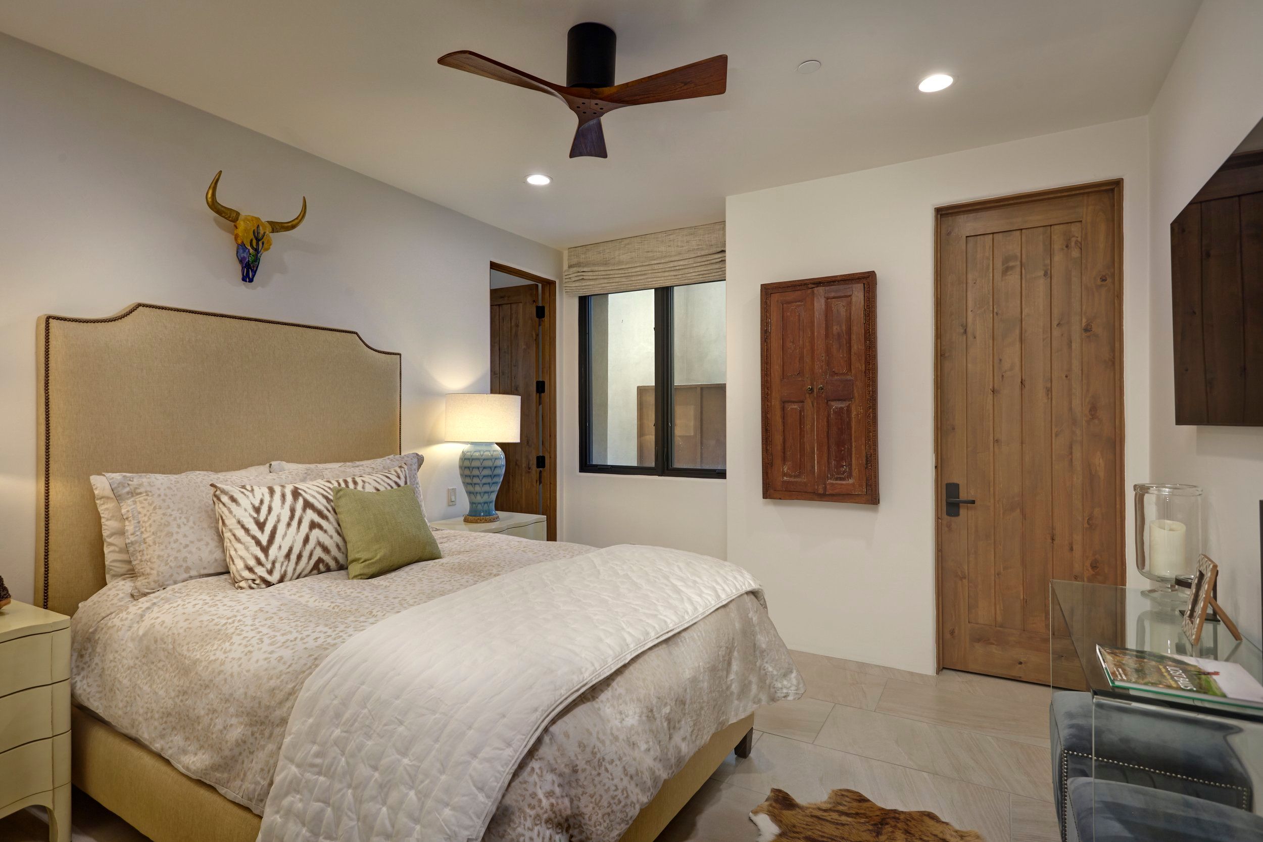 Guest bedroom with an upholstered headboard, ceiling fan and steer skull artwork
