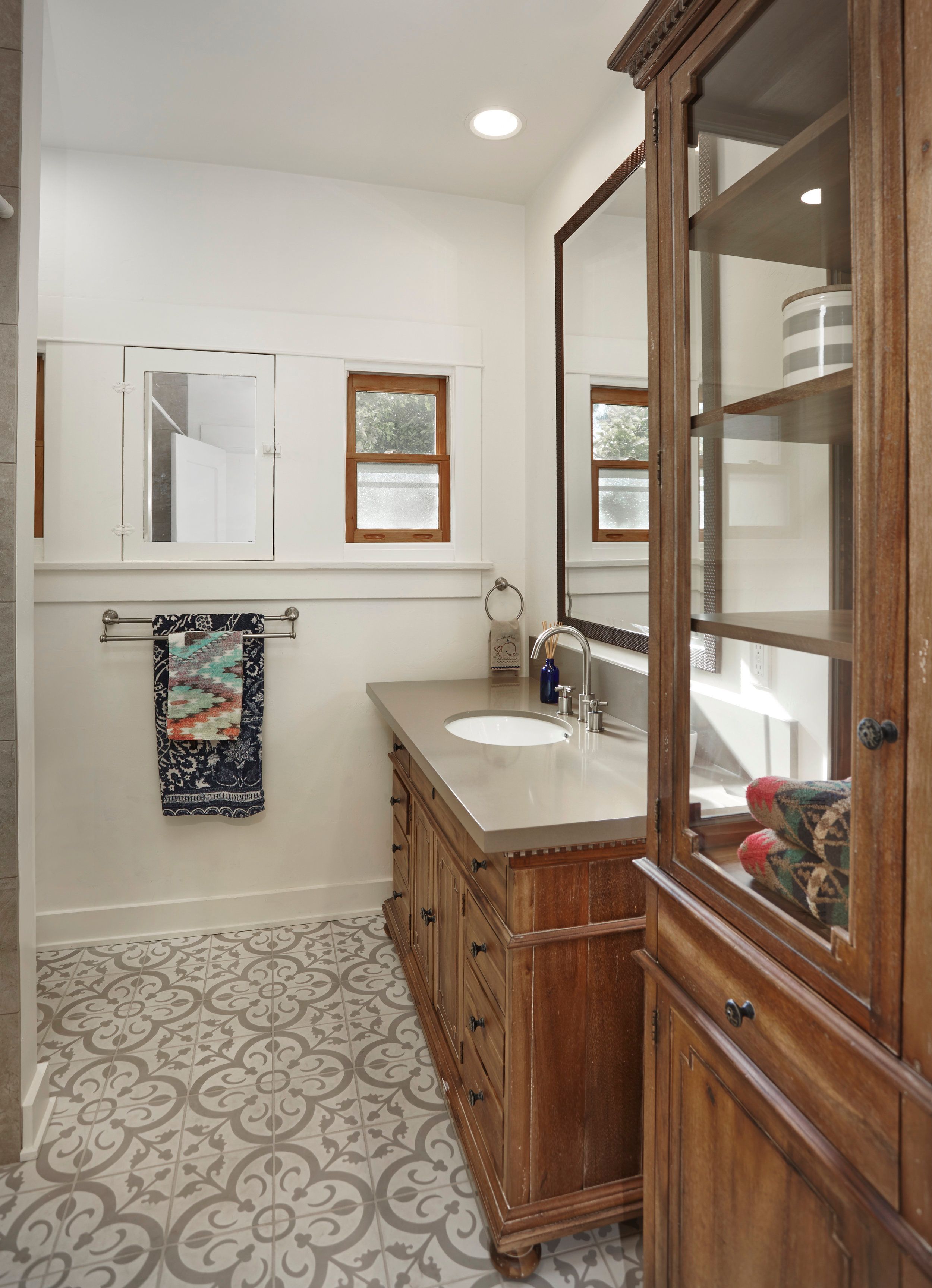 Powder room with a wood vanity, patterned cement floor tile and glass cabinet