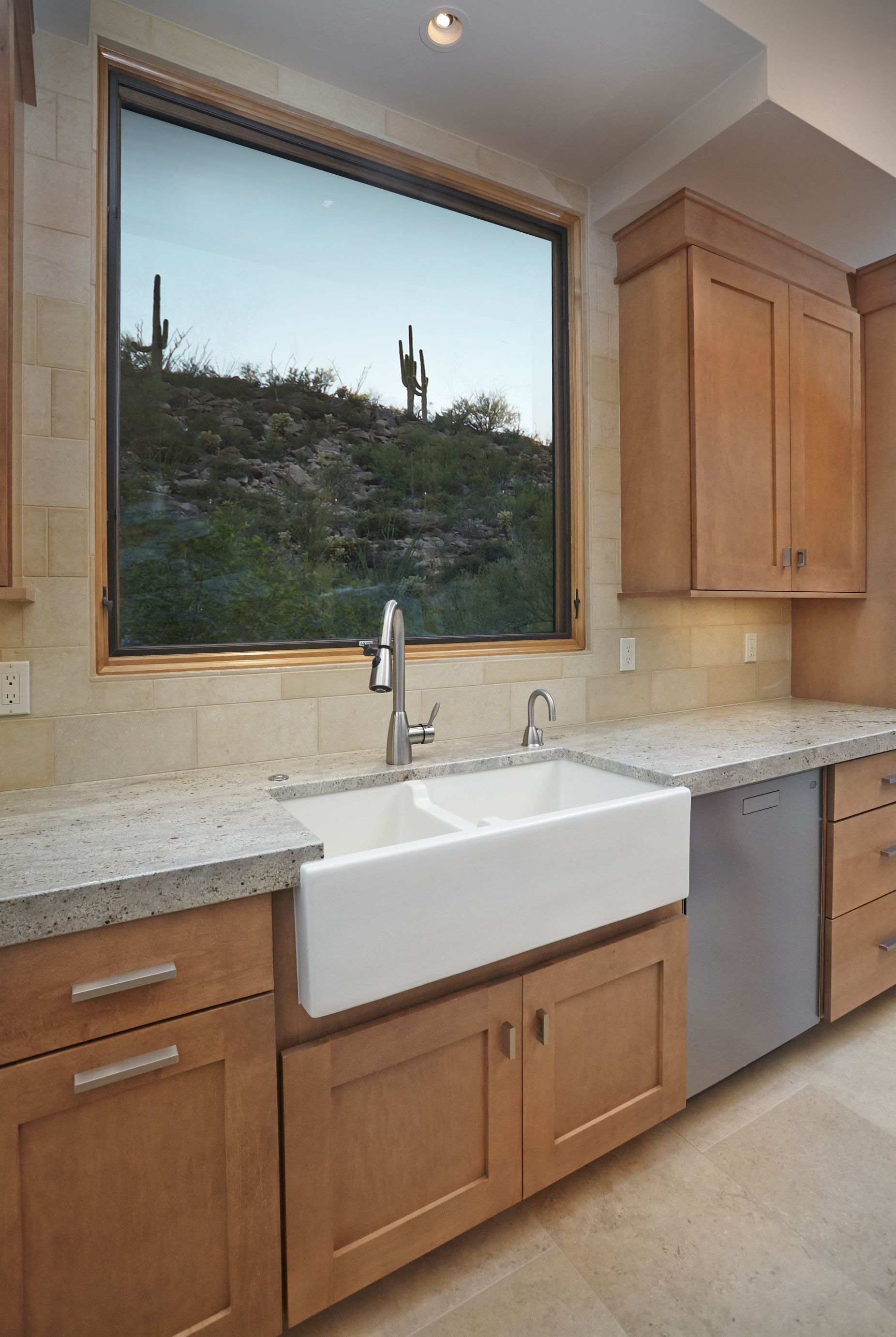 Kitchen sink with a farmhouse basin beneath a window framing saguaros