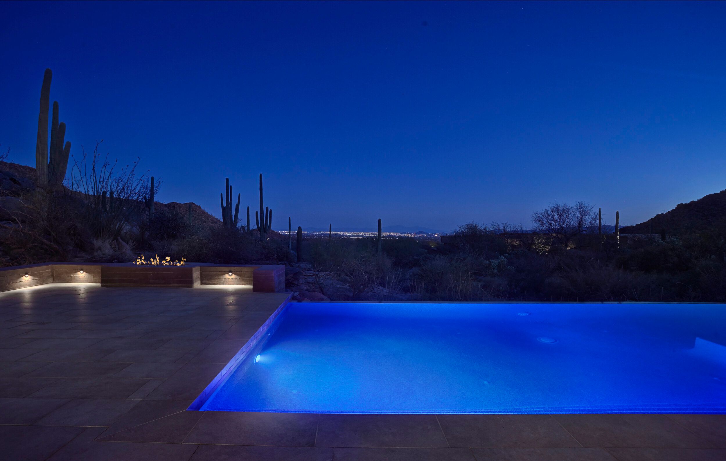 Pool lit blue at night with city lights on the horizon