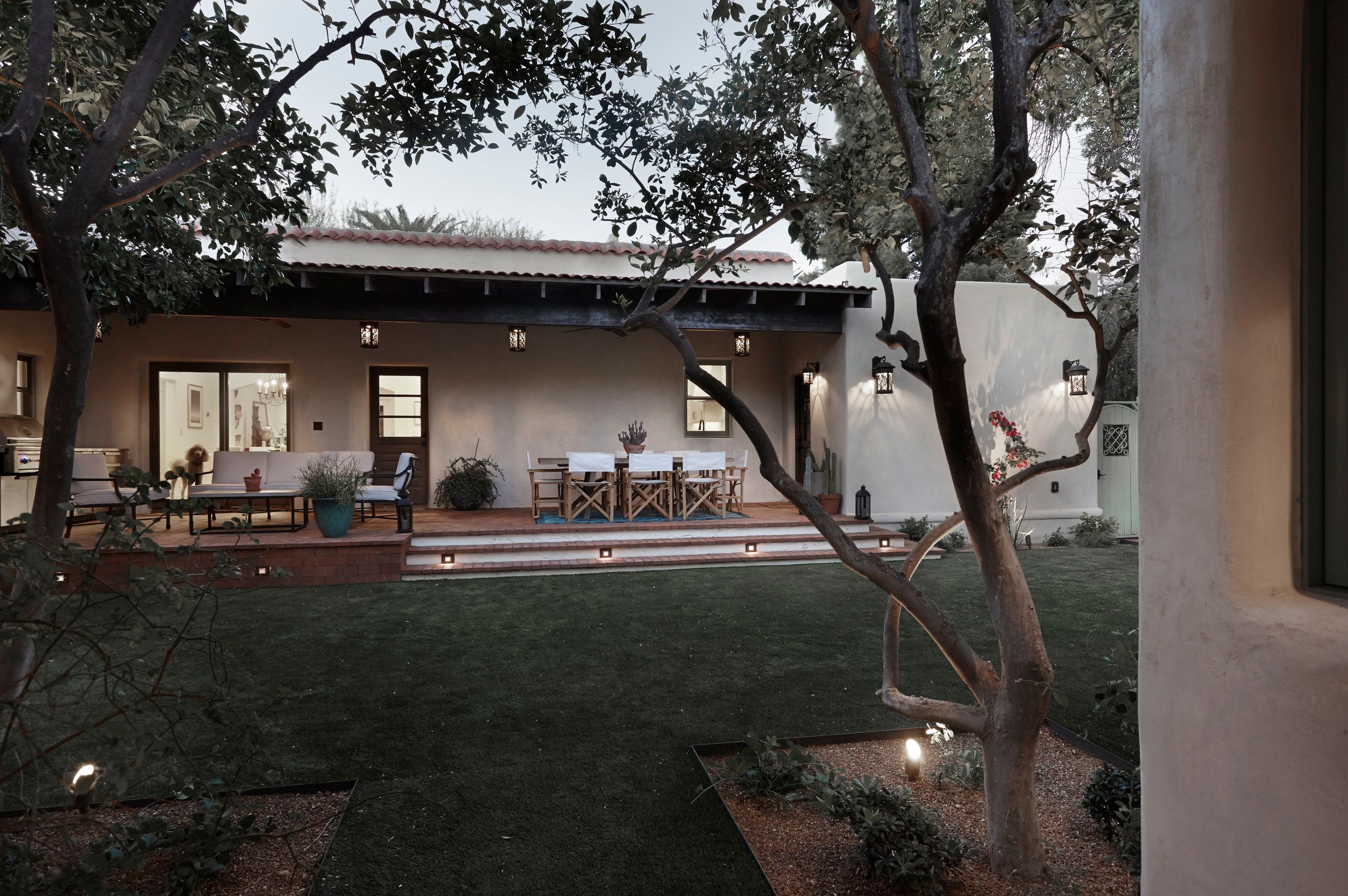 Rear courtyard at dusk with a lawn, mature trees and a lit covered porch