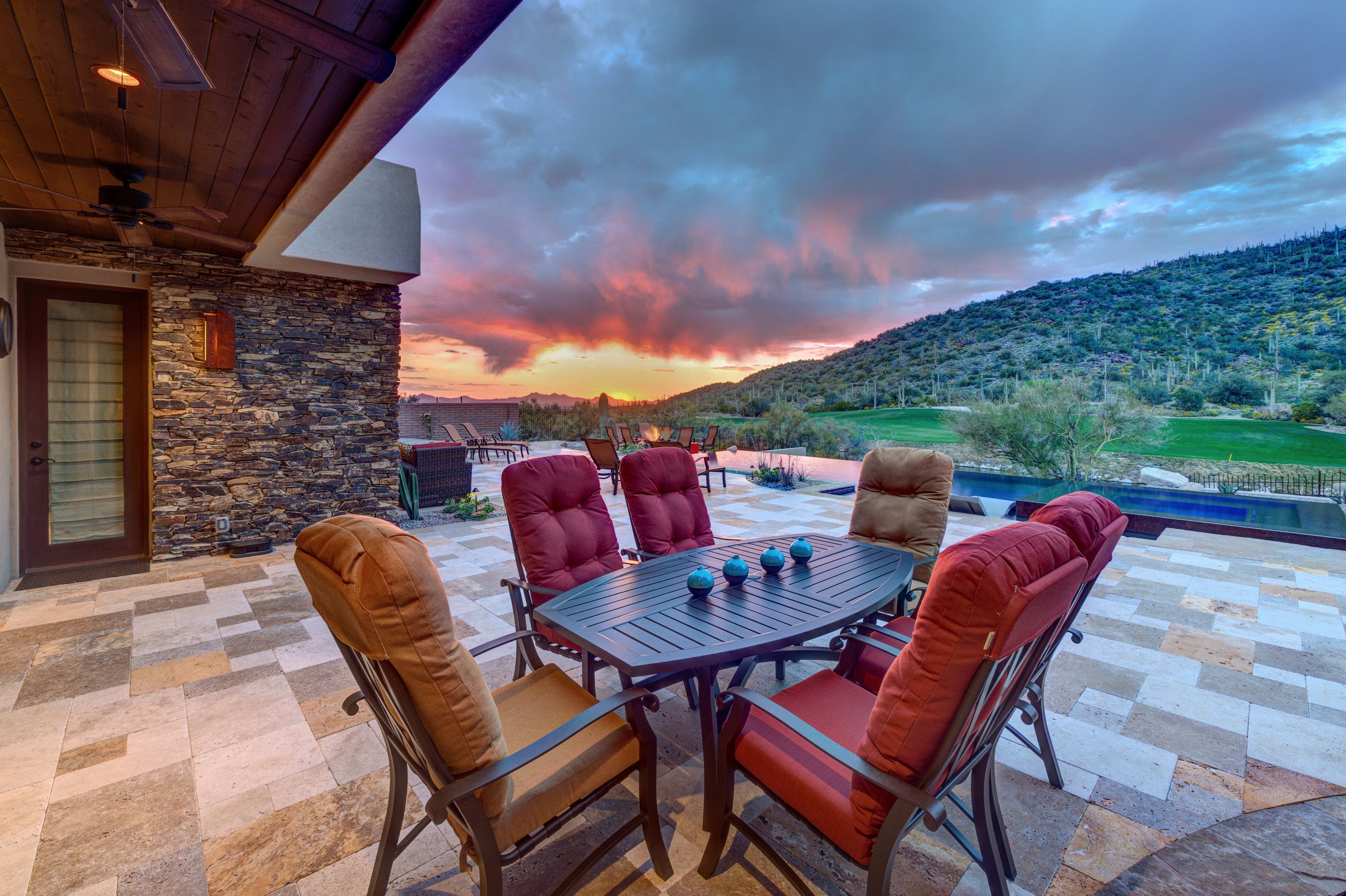 Covered patio with cushioned dining chairs overlooking the golf course at sunset