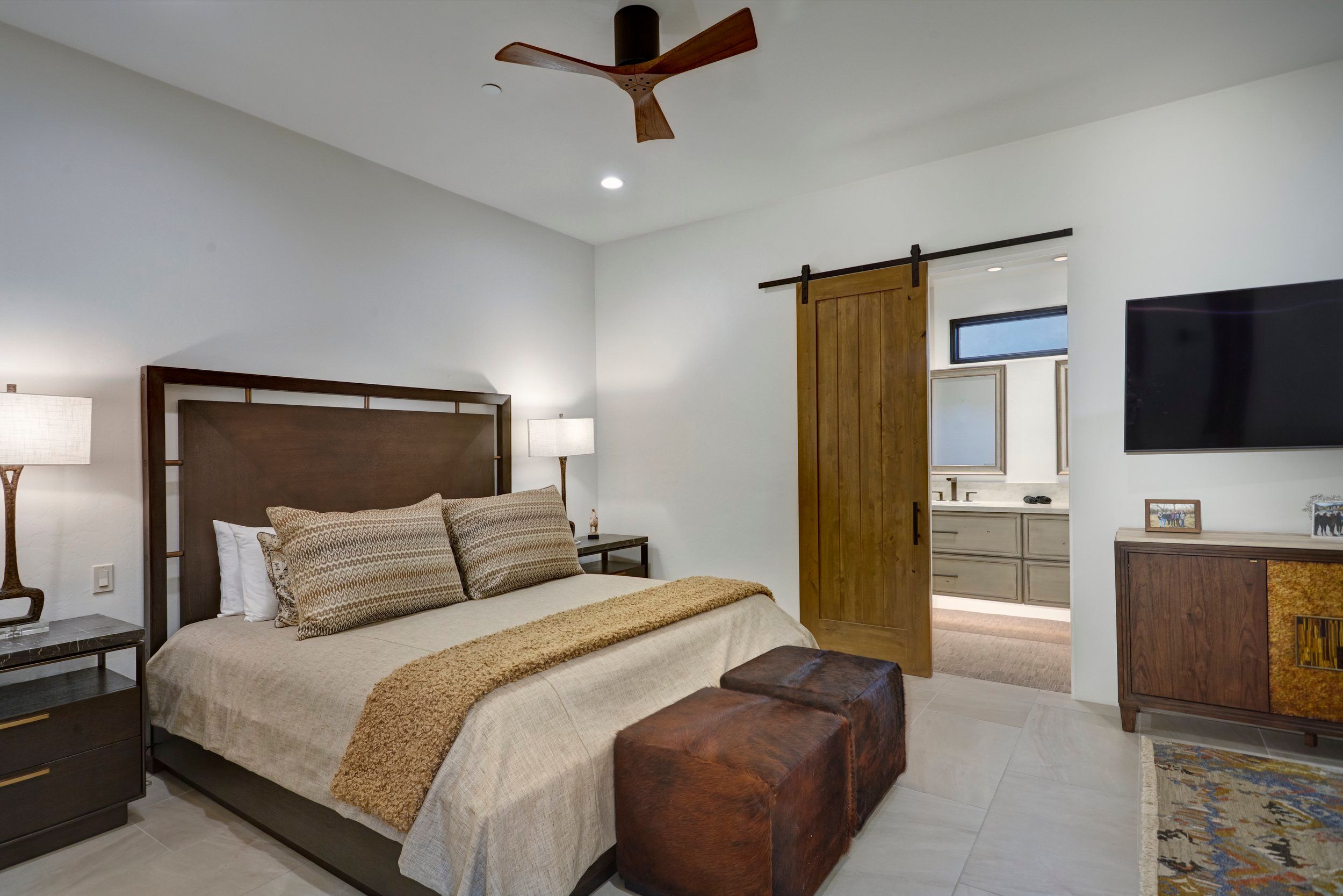 Guest bedroom with a leather bench, sliding barn door to the ensuite and mounted television