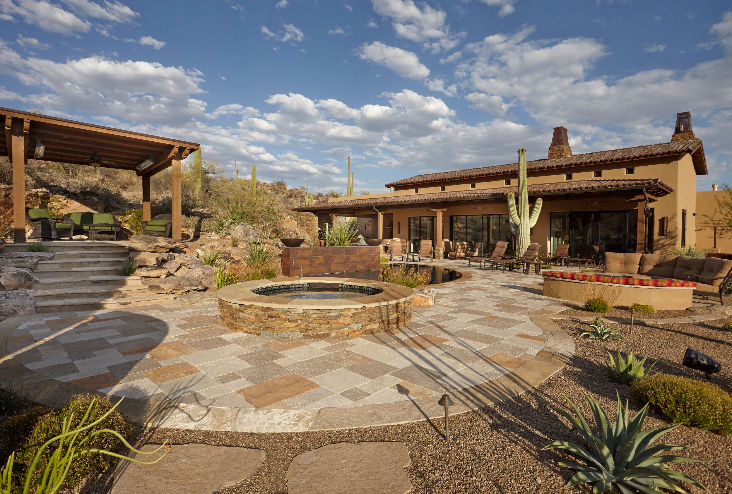 Travertine terrace with a raised stone spa and ramada beside the house