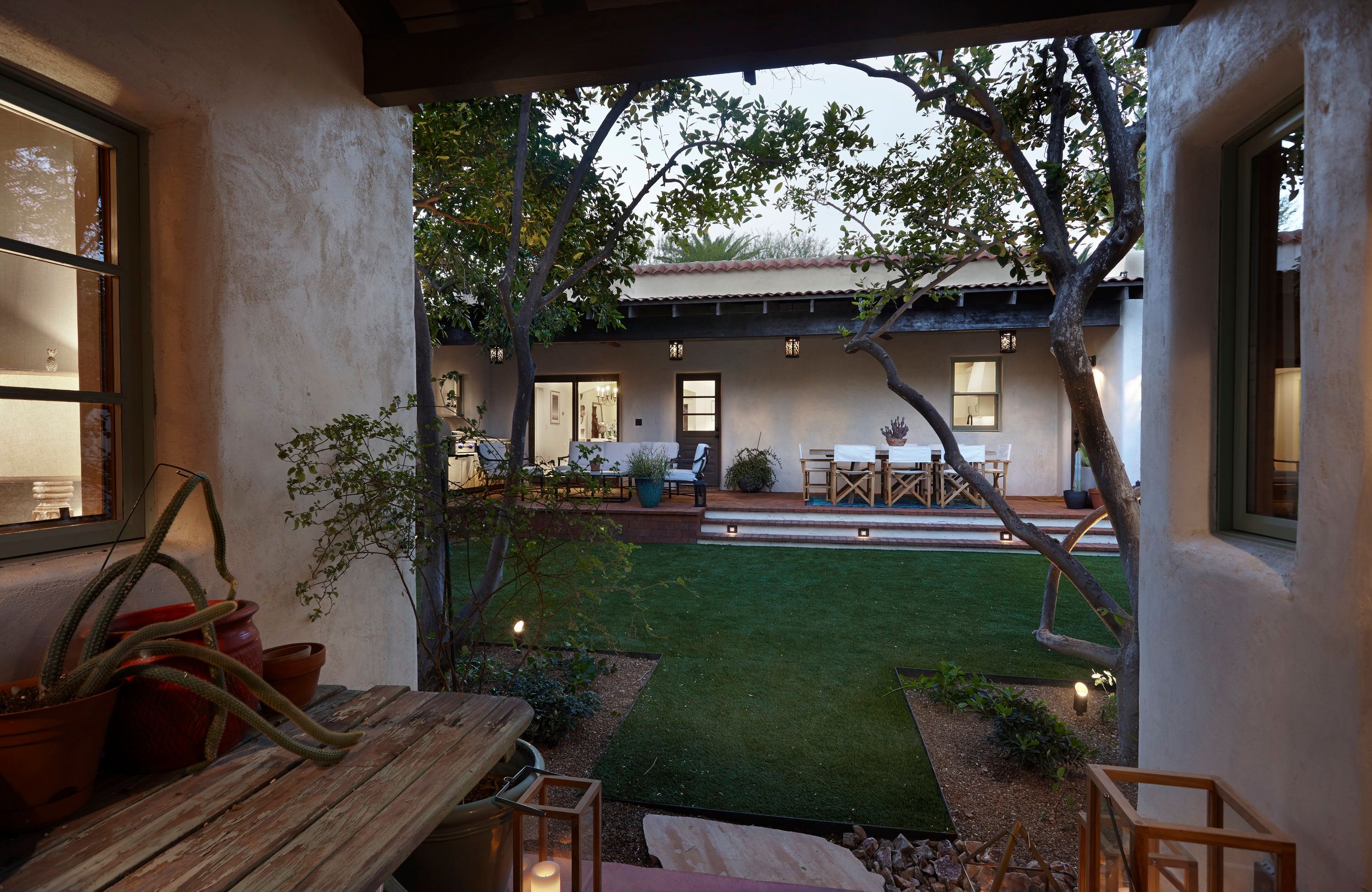 View from the porch across the courtyard lawn to the lit house at twilight