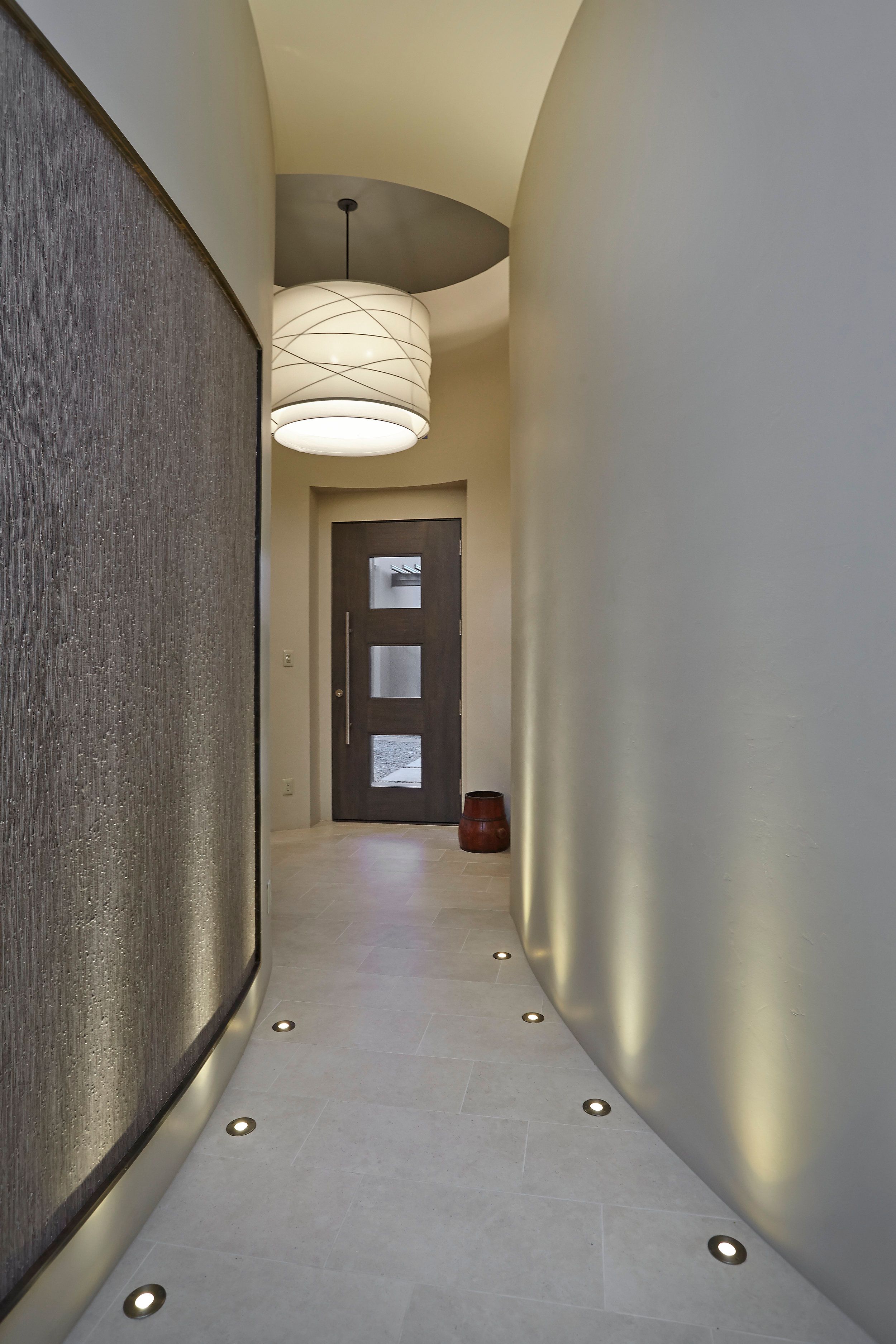 Curved entry hall with a grasscloth wall, uplighting and glass front door