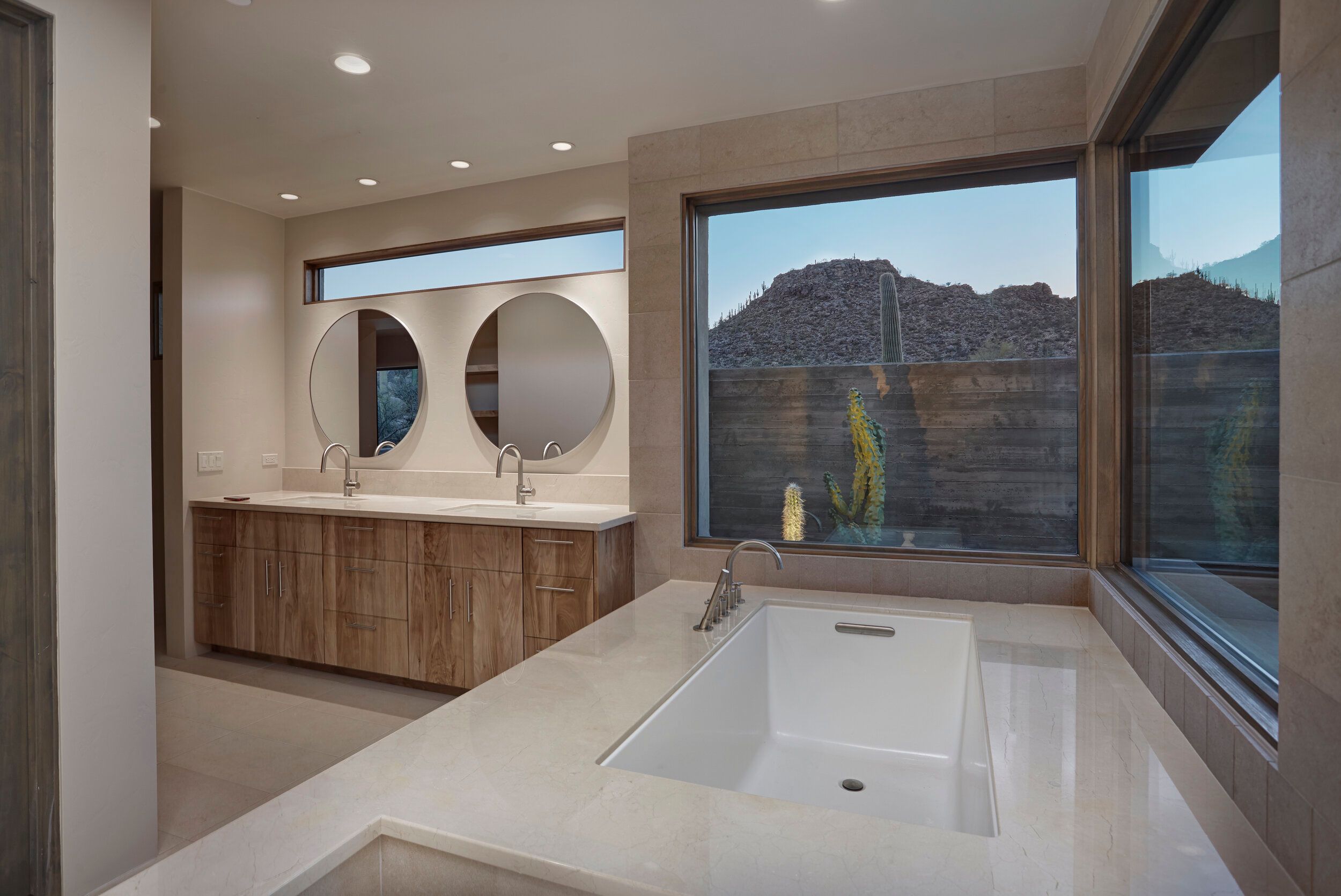 Primary bathroom with round mirrors, twin vanities and a window over the tub