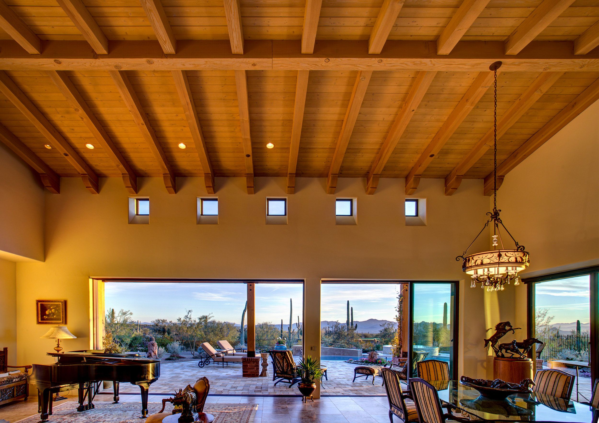 Living room at dusk with an exposed-beam ceiling and glass wall framing saguaros