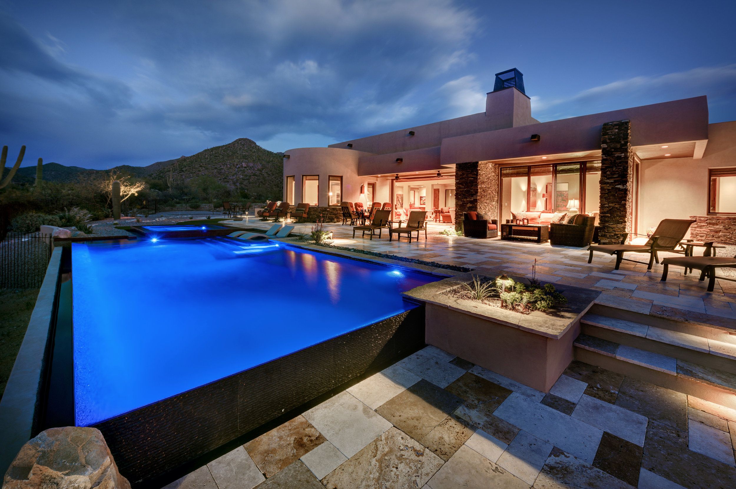 Negative-edge pool lit blue at dusk with the house glowing behind