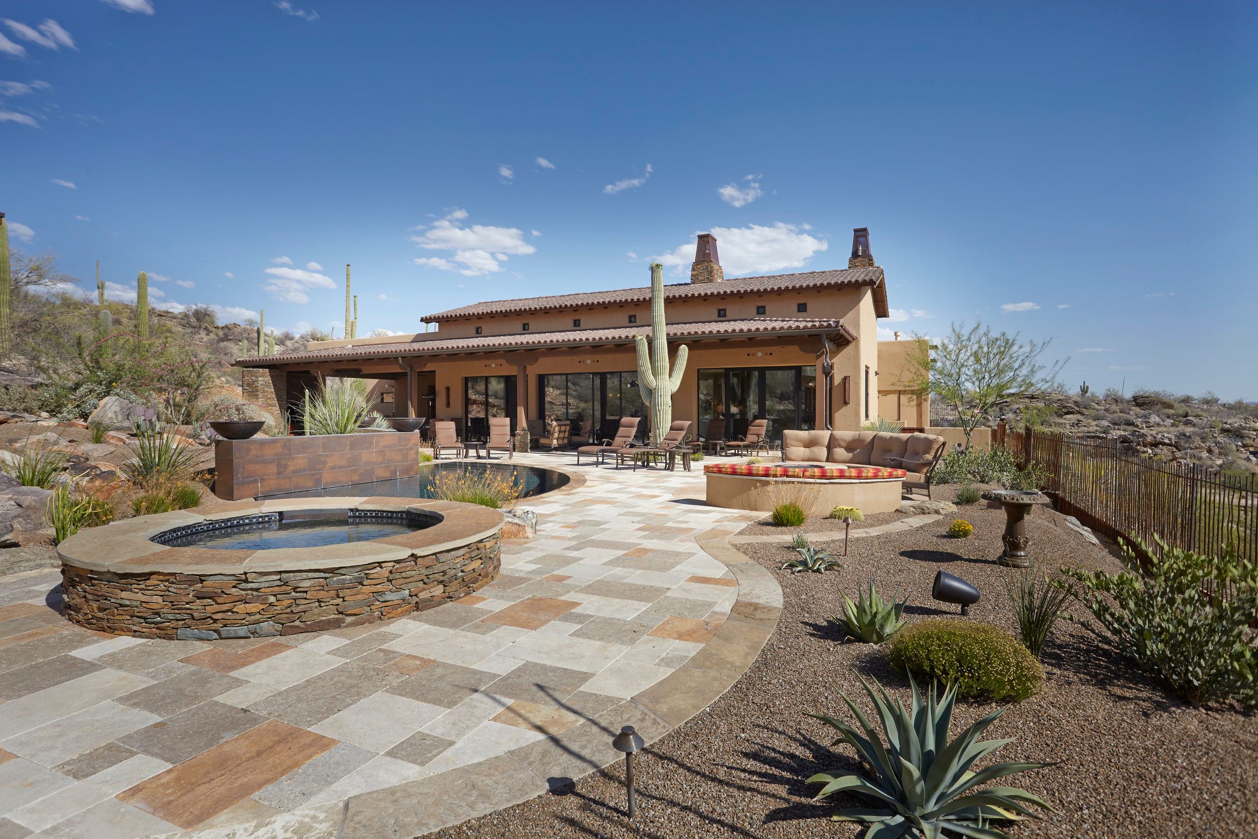 Rear elevation with a stone spa, patio seating and desert plantings