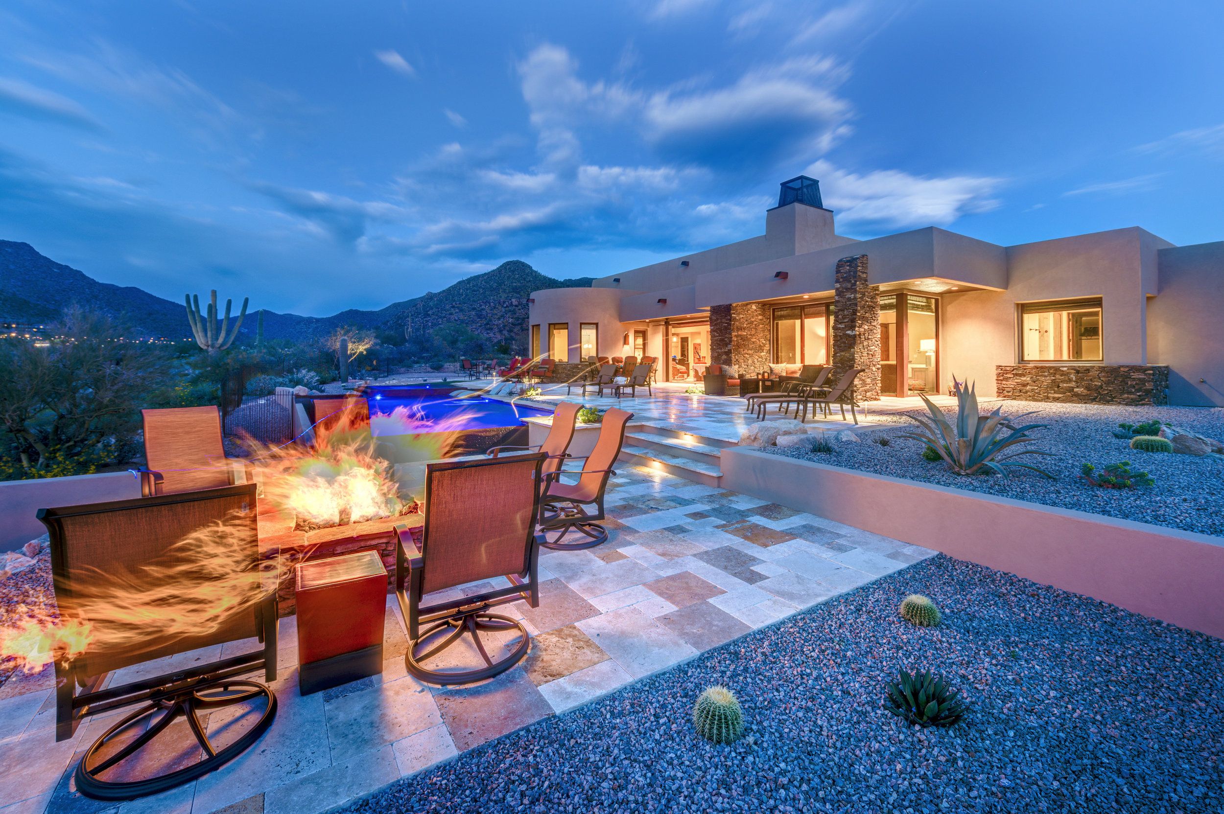 Fire pit seating on the terrace at twilight beside the lit pool
