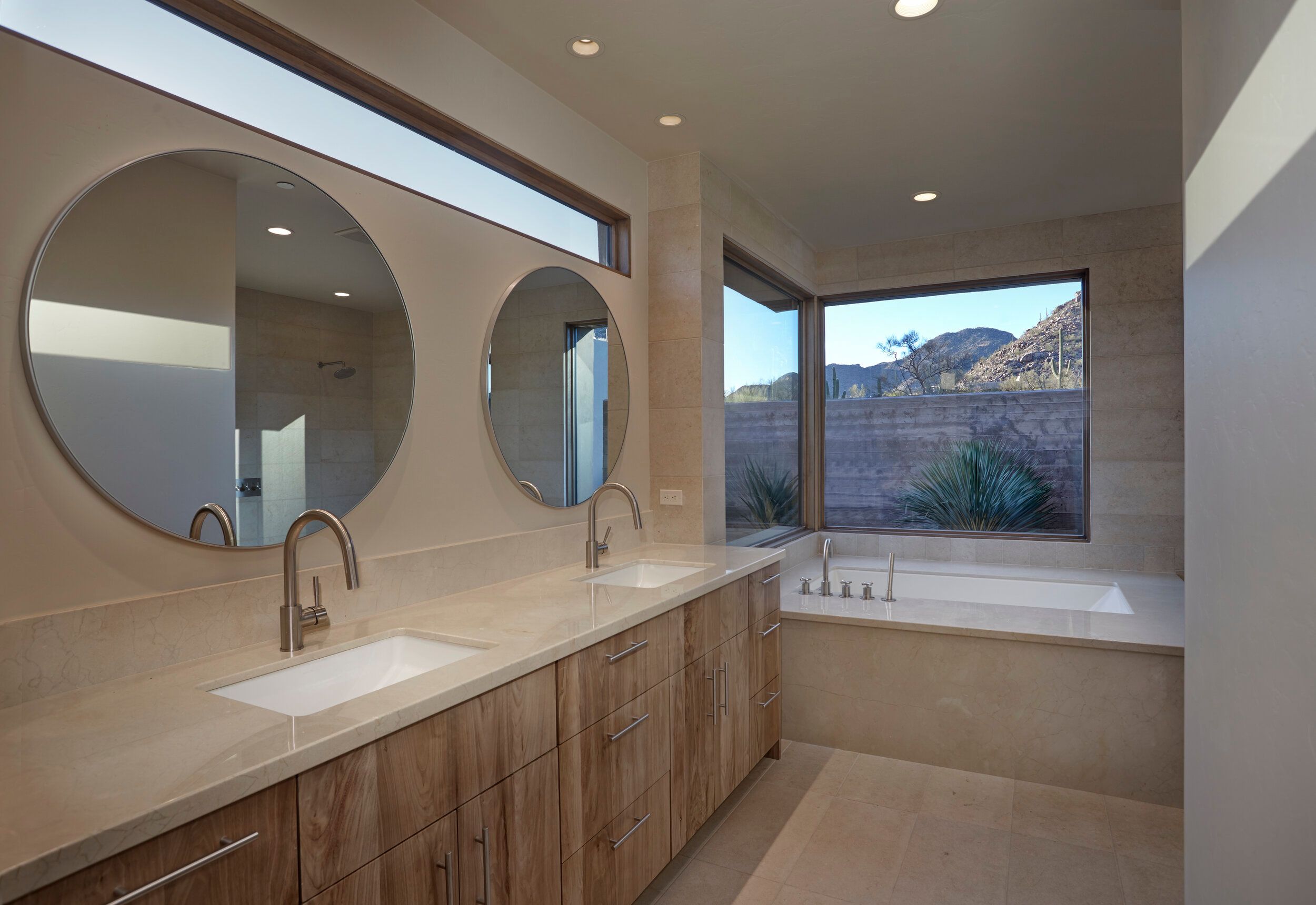 Vanity with round mirrors and a soaking tub beneath a desert window