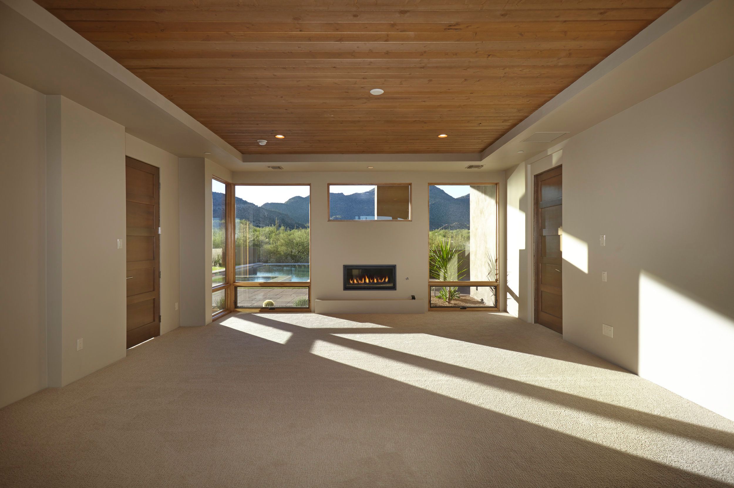 Bedroom with a wood-plank ceiling looking through to the fireplace and pool