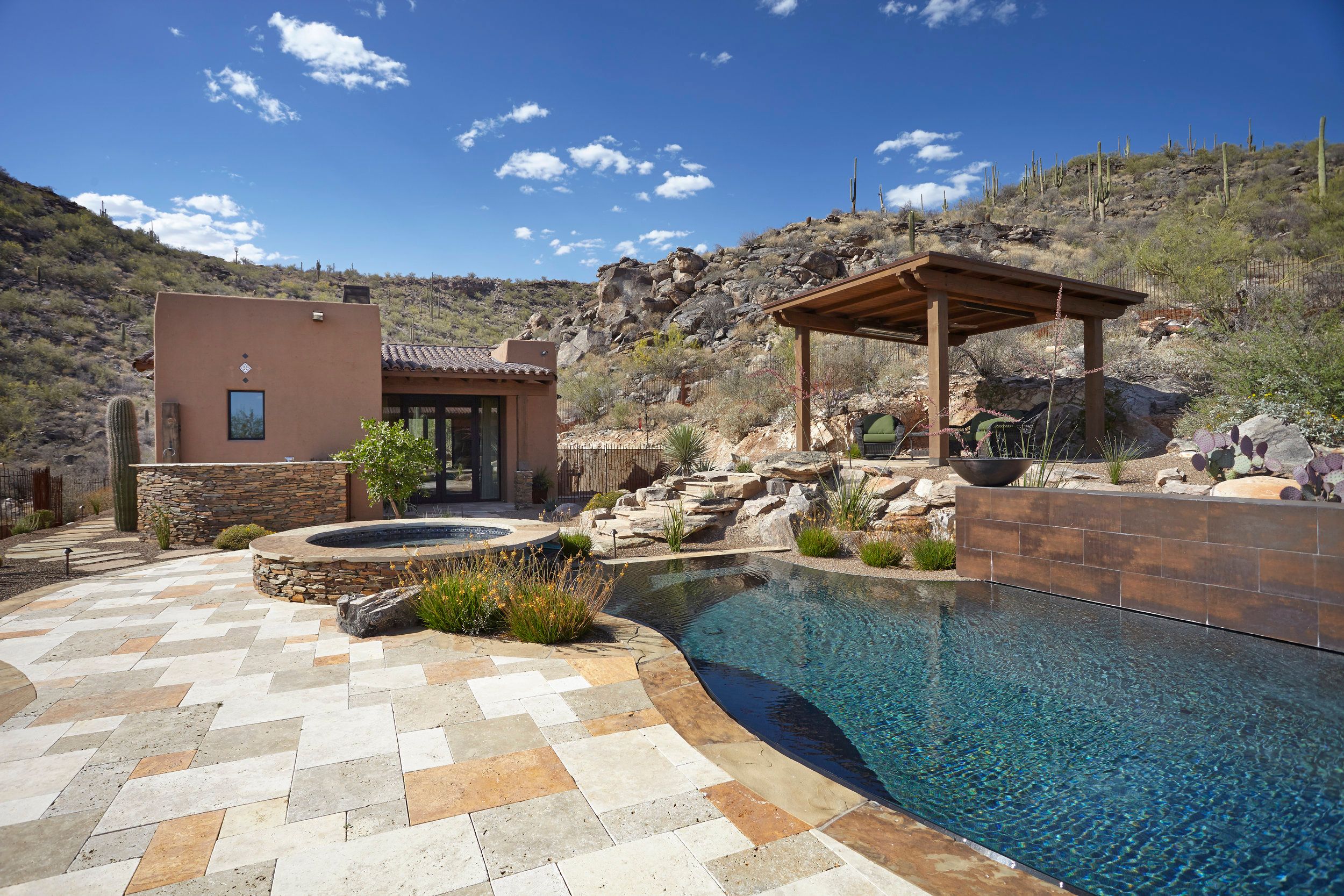 Pool and spa on a travertine deck with a timber ramada and casita beyond