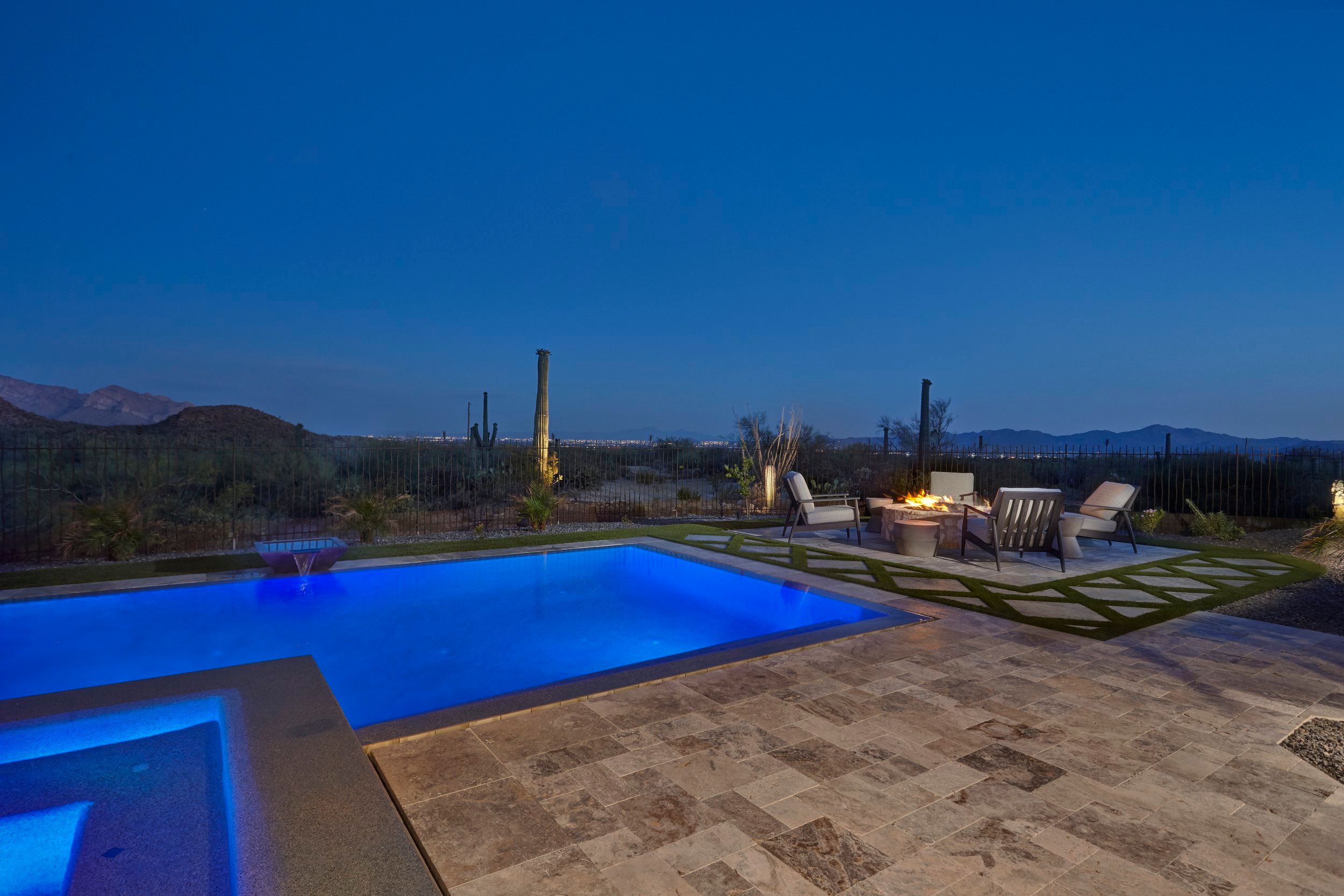 Pool lit blue at dusk with a fire feature and mountains on the horizon