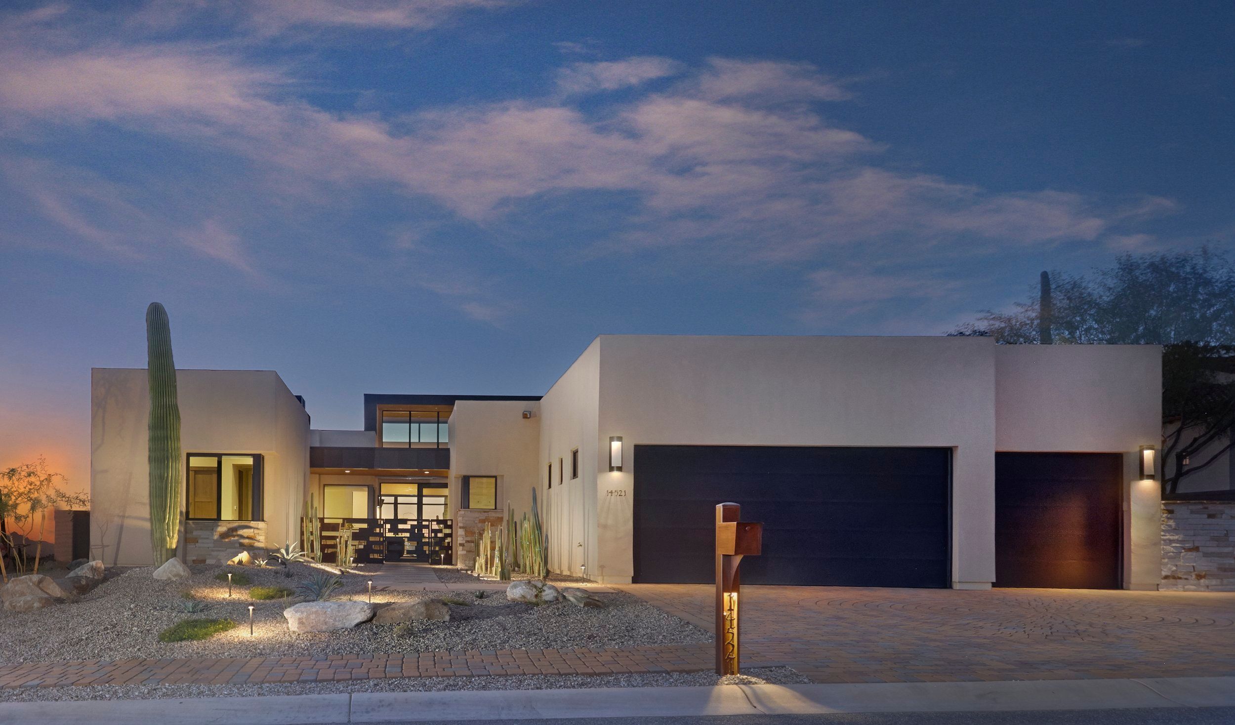 Front elevation at dusk with a lit garage, saguaros and contemporary massing