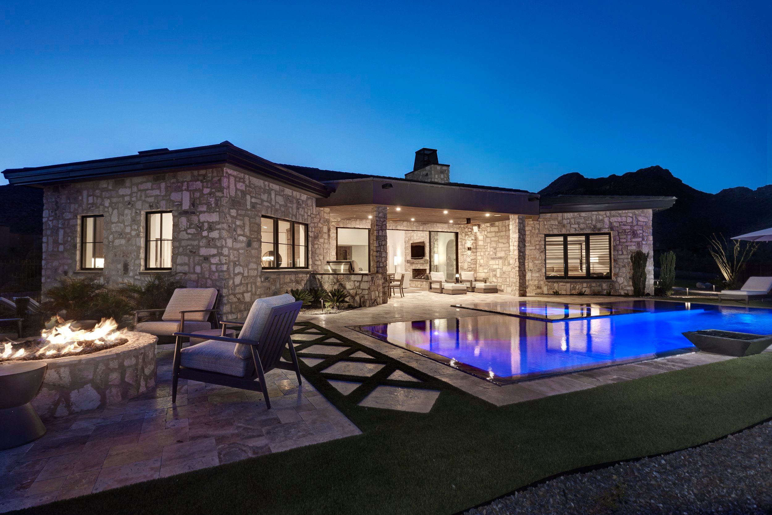 Rear elevation at dusk with a fire pit seating group beside the lit negative-edge pool