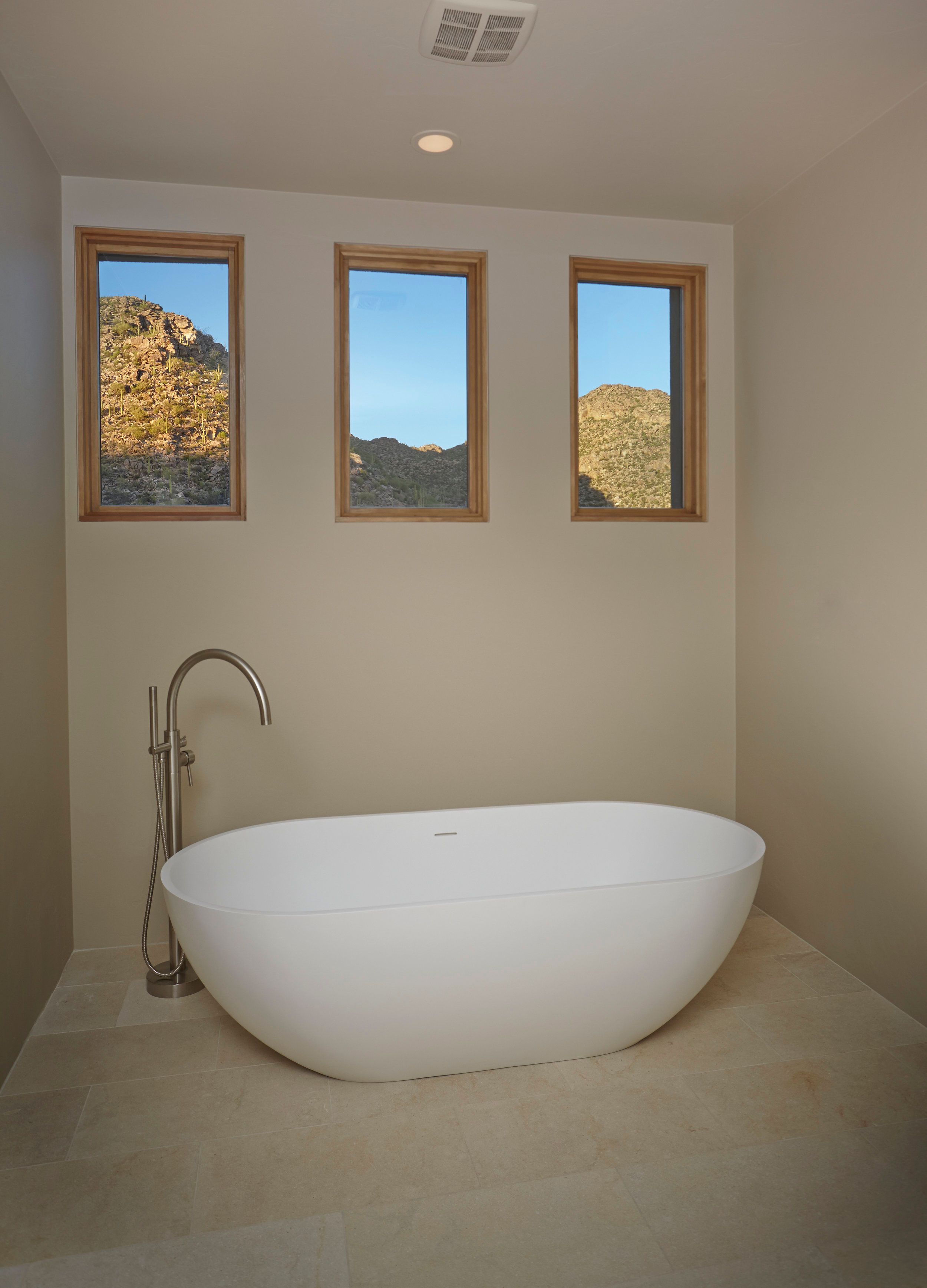 Freestanding soaking tub beneath three square windows framing the mountains