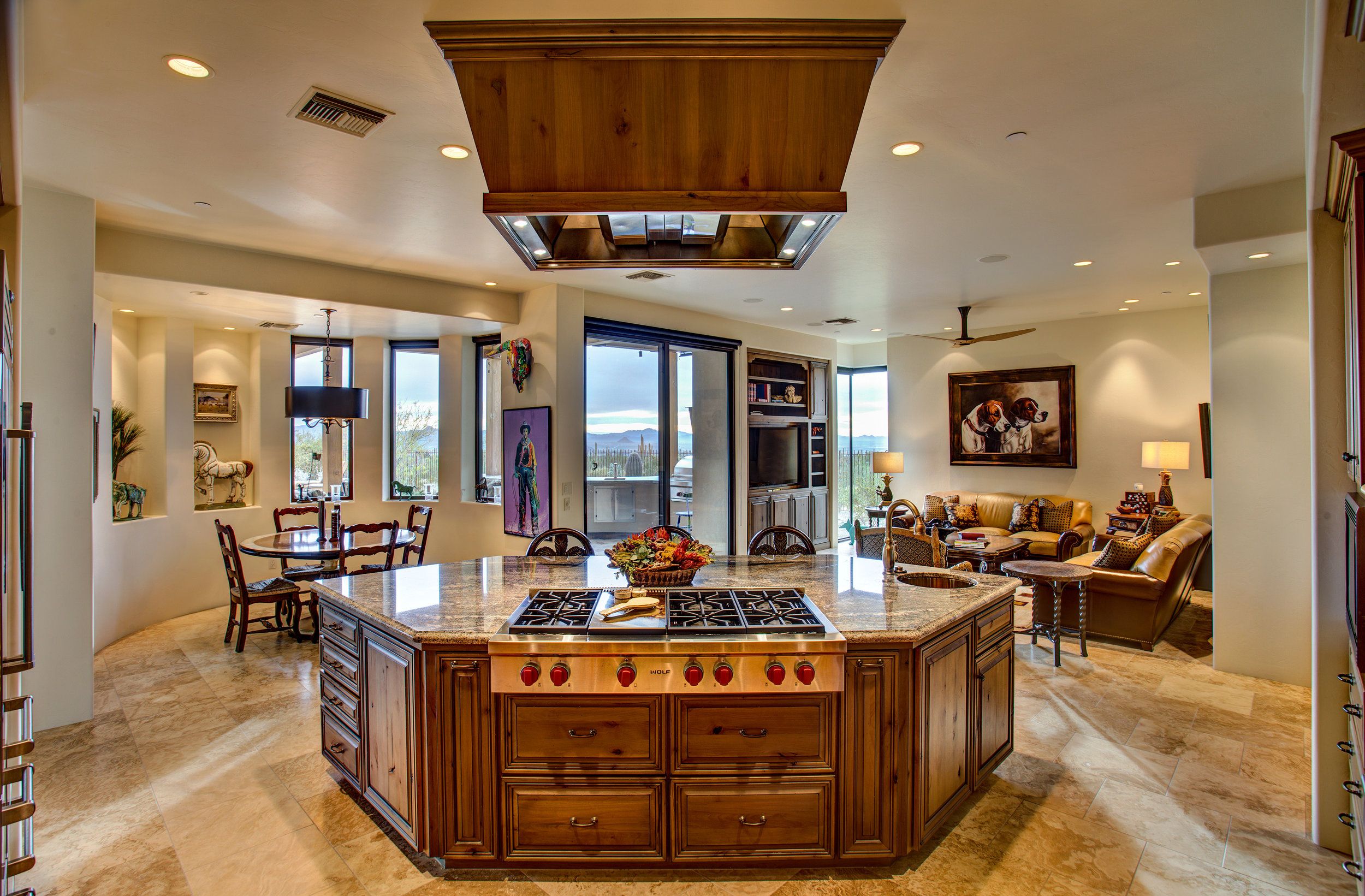 Kitchen island with a gas cooktop and wood hood, open to the family room beyond