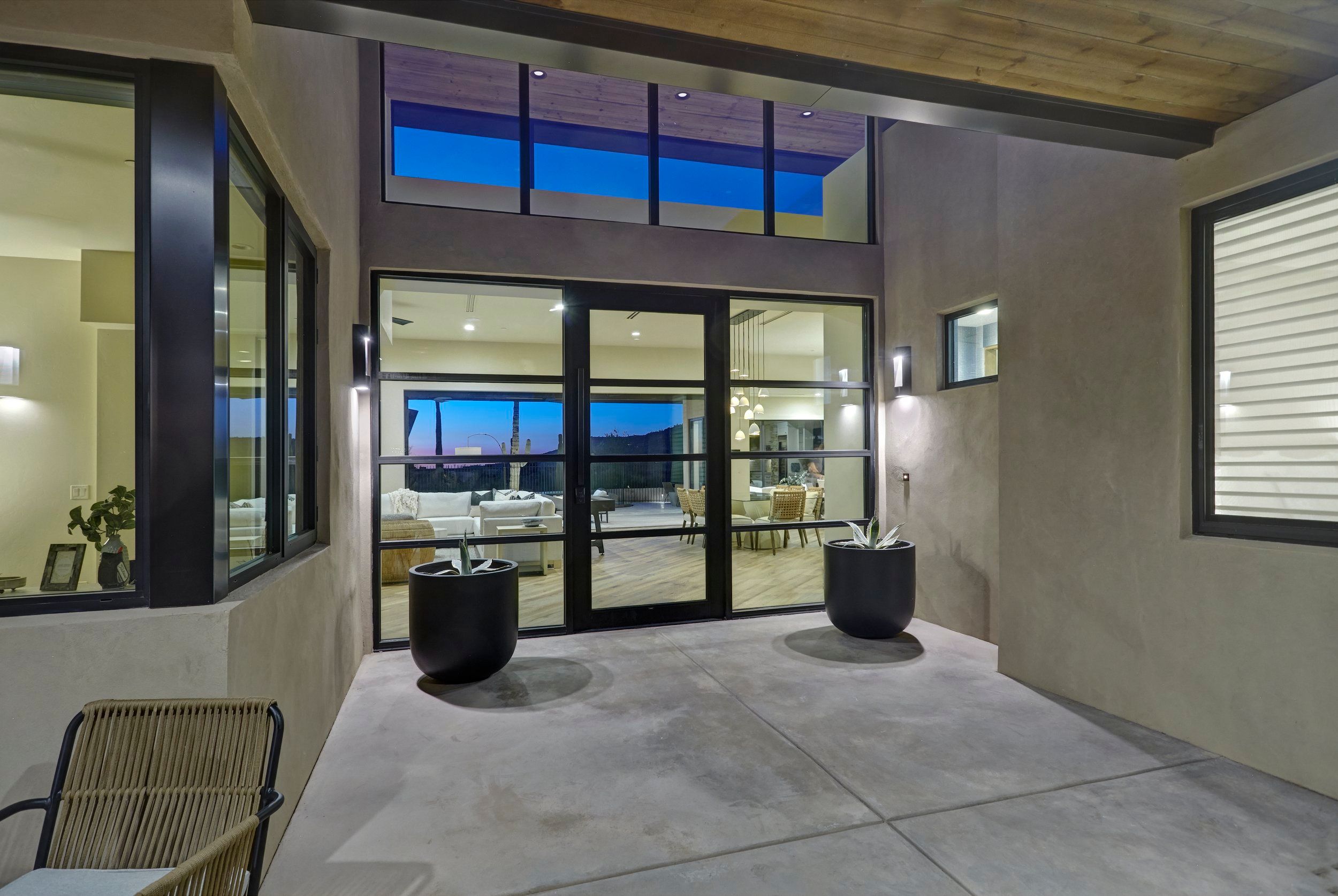 Side courtyard looking through full-height glass into the lit living room
