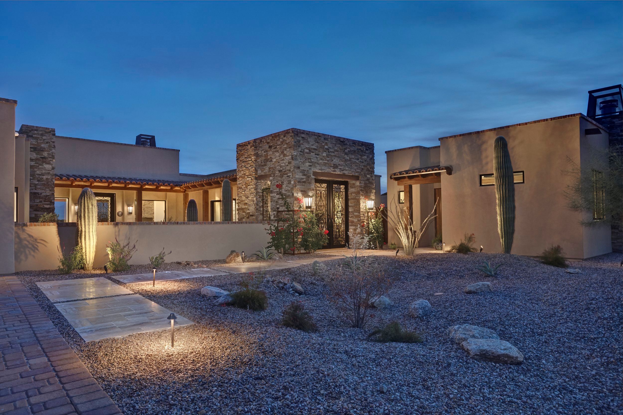 Stone and stucco entry courtyard lit at twilight with desert landscaping