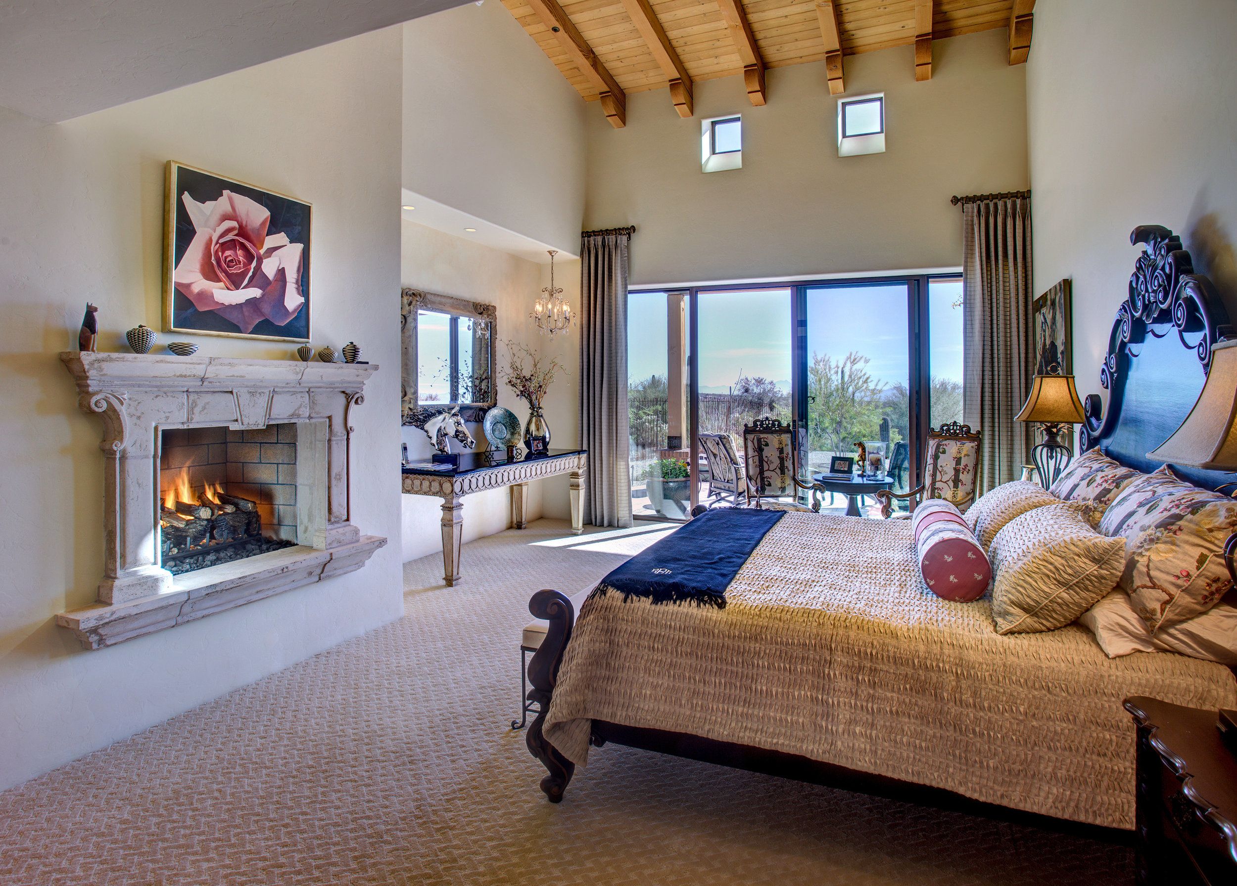 Primary bedroom with a carved stone fireplace, beamed ceiling and patio access