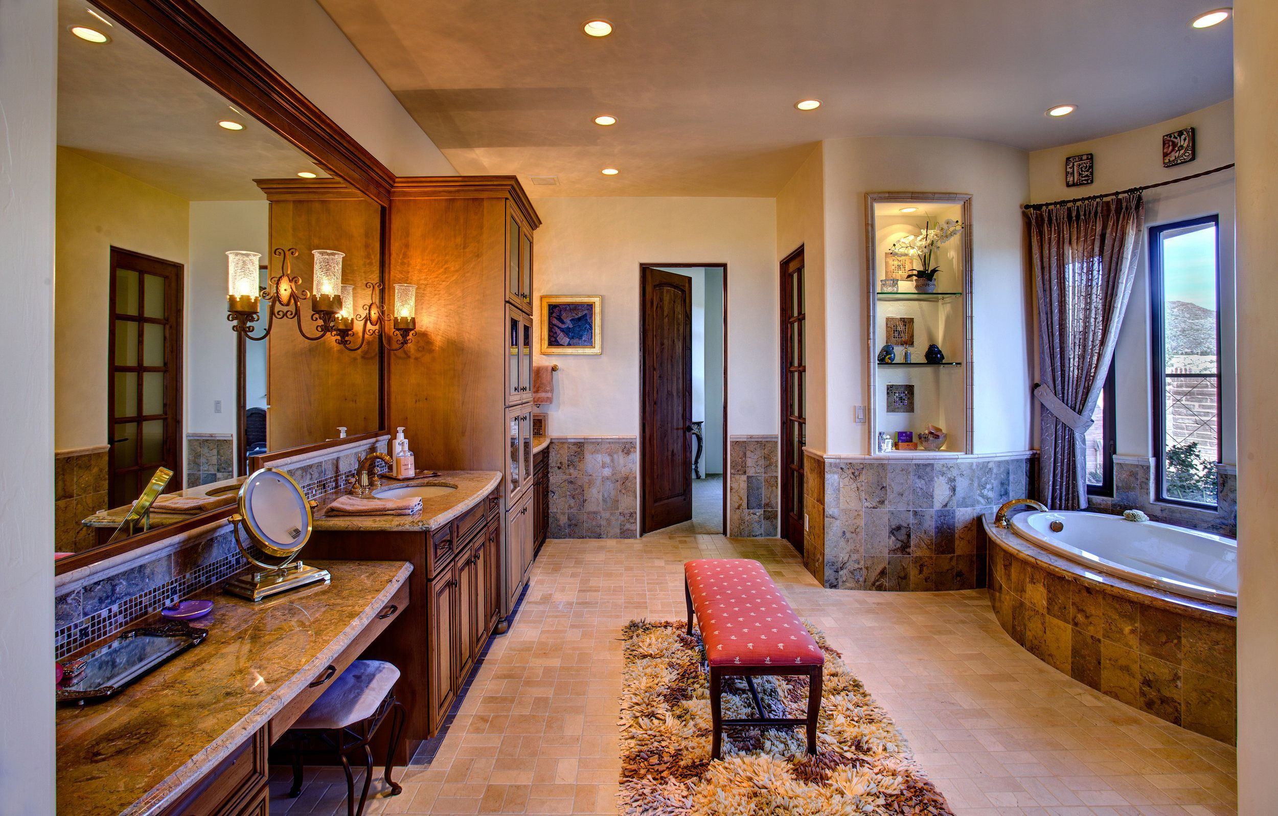 Primary bathroom with a travertine-surround soaking tub, double vanity and upholstered bench