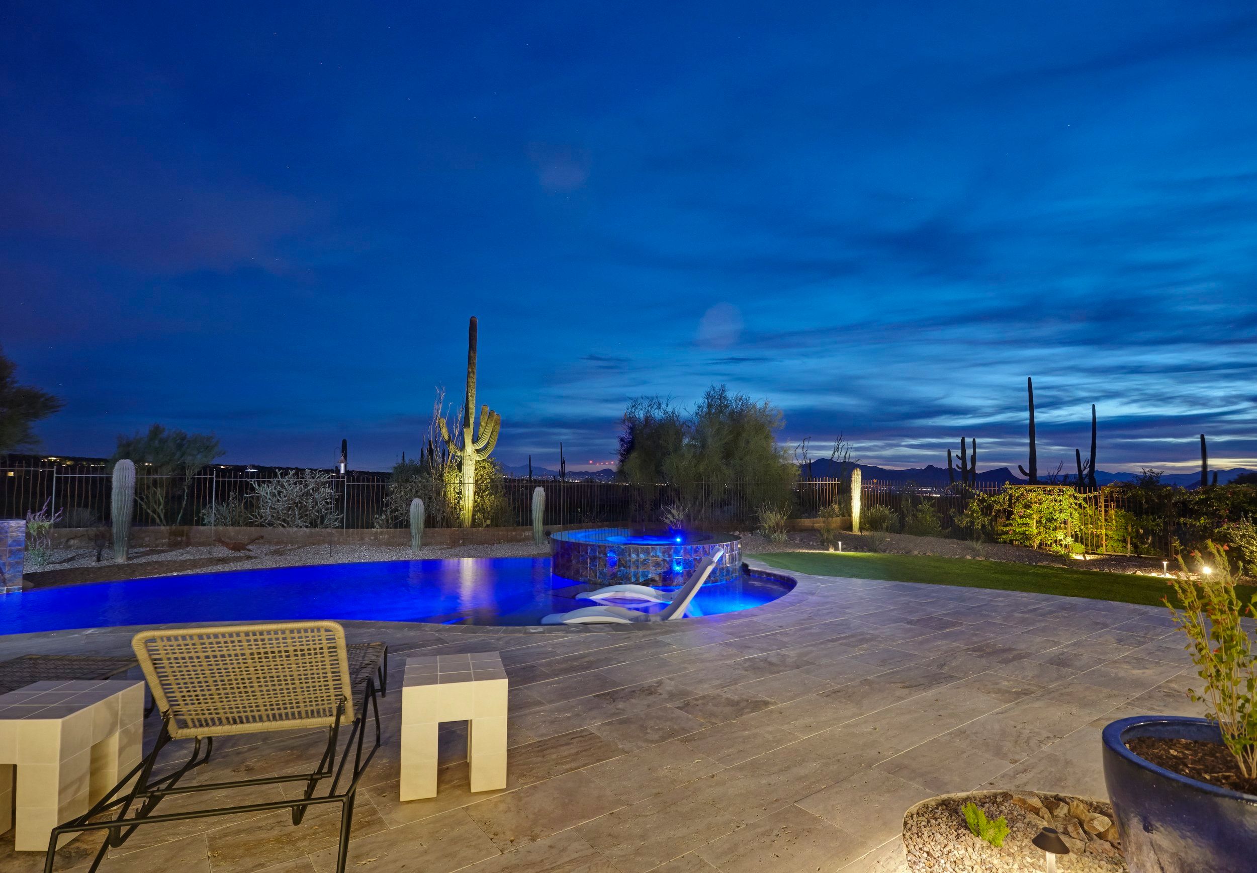 Pool lit blue at twilight with saguaros and lounge seating on the travertine deck