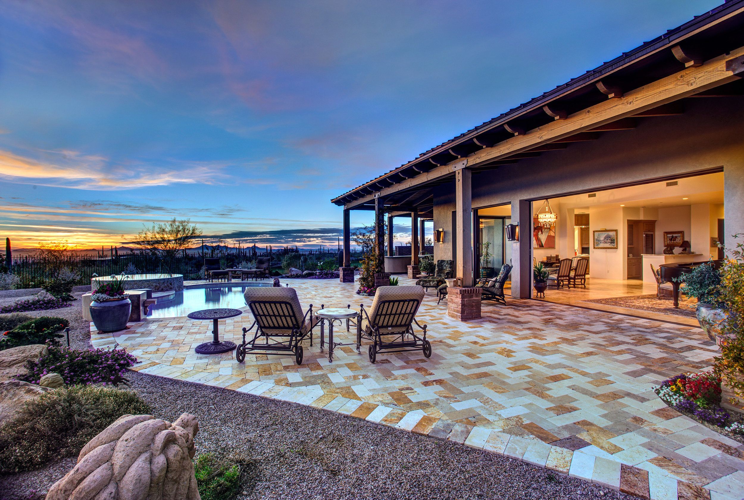 Rear patio at sunset with lounge seating and the pool beyond the paver deck
