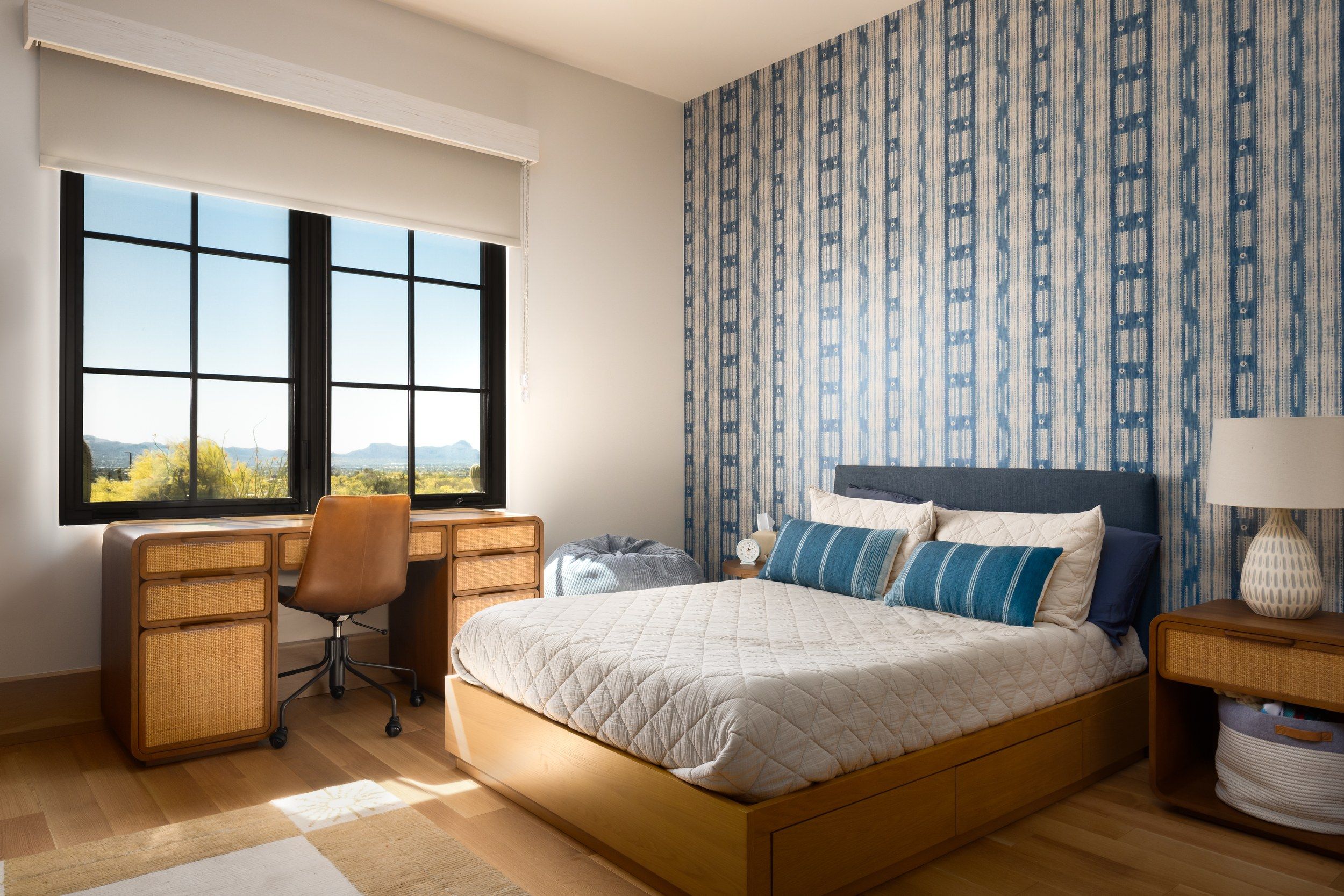 Guest bedroom with a blue patterned wall, upholstered bed and writing desk