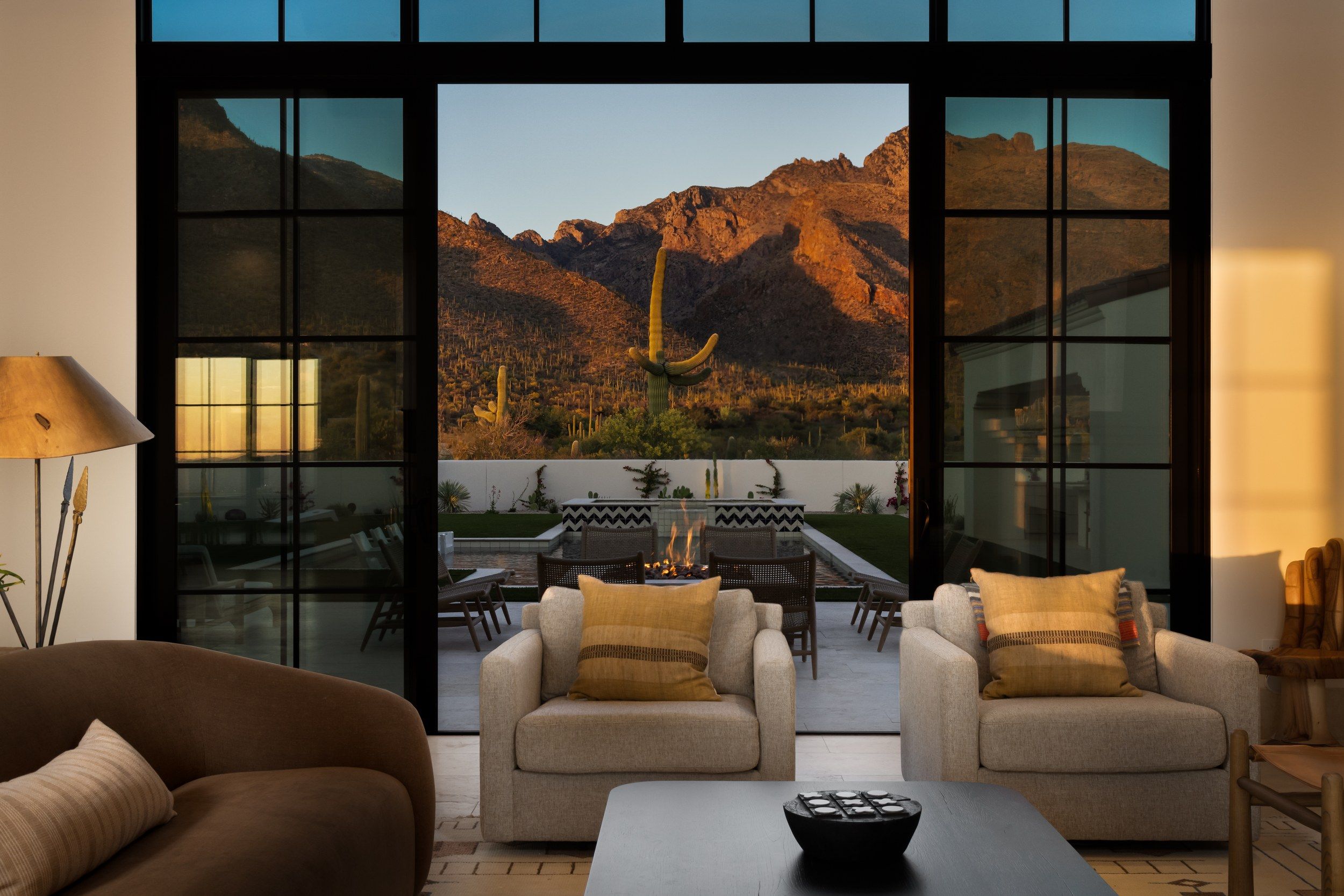 Living room at dusk framing a lit saguaro and the mountains through steel windows
